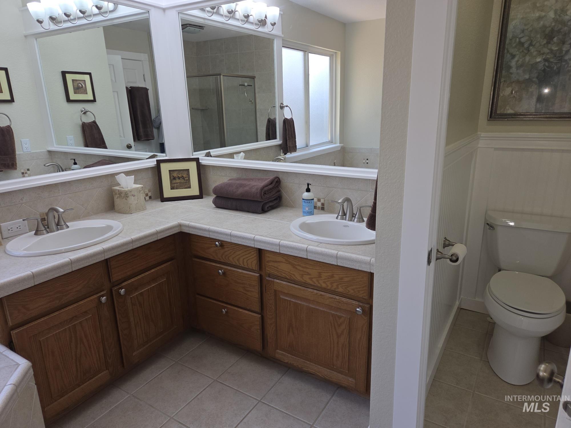 Bathroom with a stall shower, light tile patterned floors, double vanity, and wainscoting