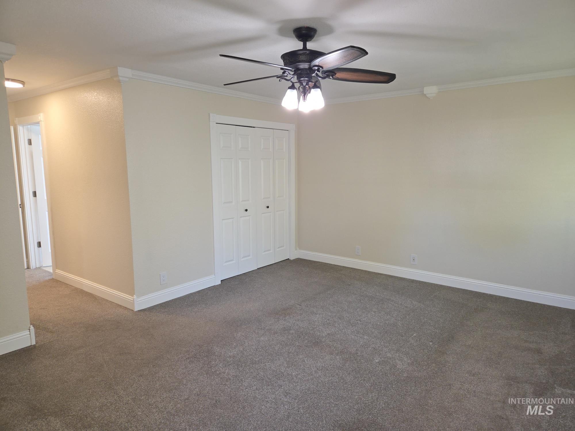 Unfurnished bedroom with dark colored carpet, ornamental molding, a closet, and a ceiling fan