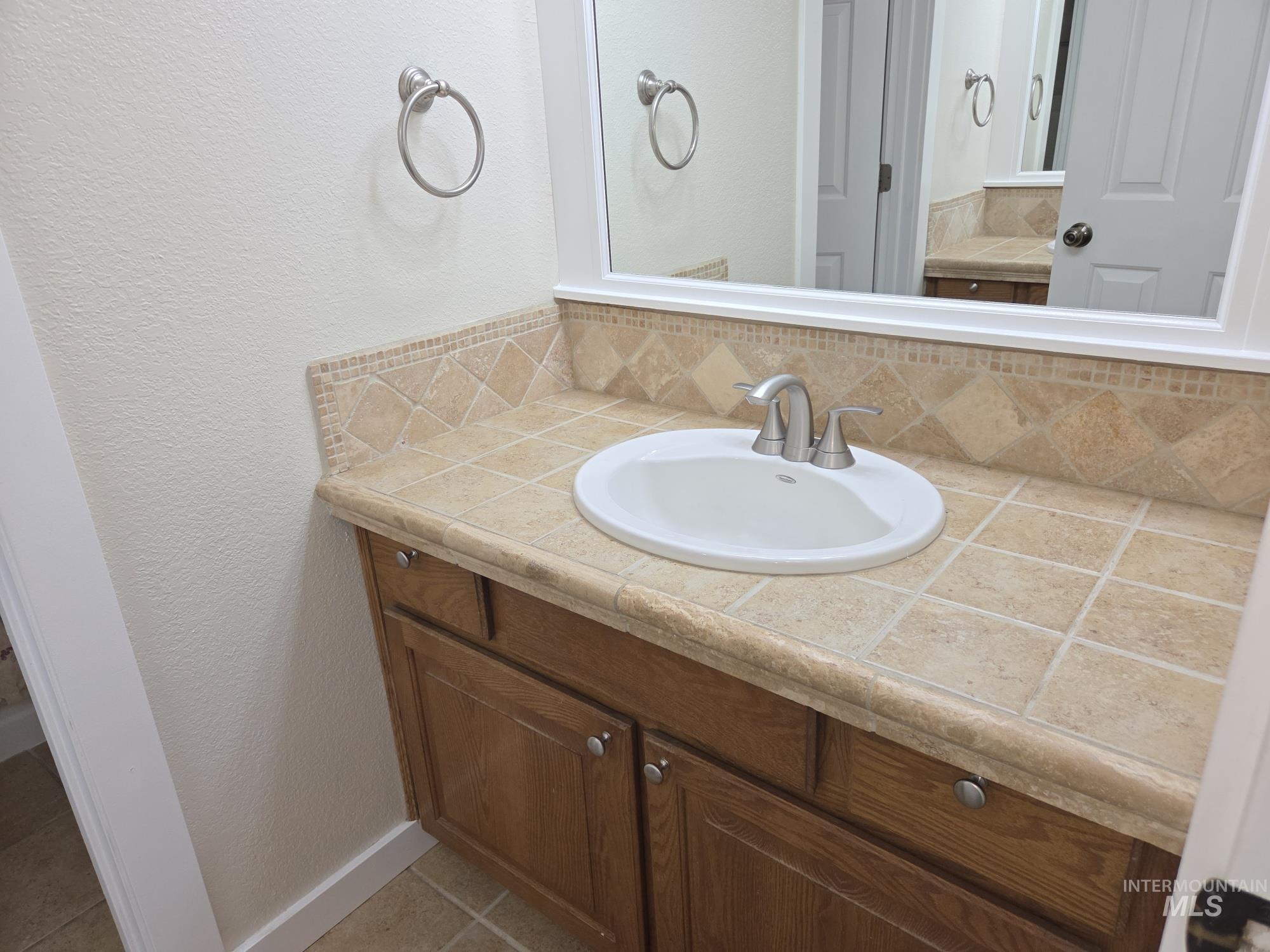 Bathroom featuring a textured wall, vanity, decorative backsplash, and light tile patterned floors