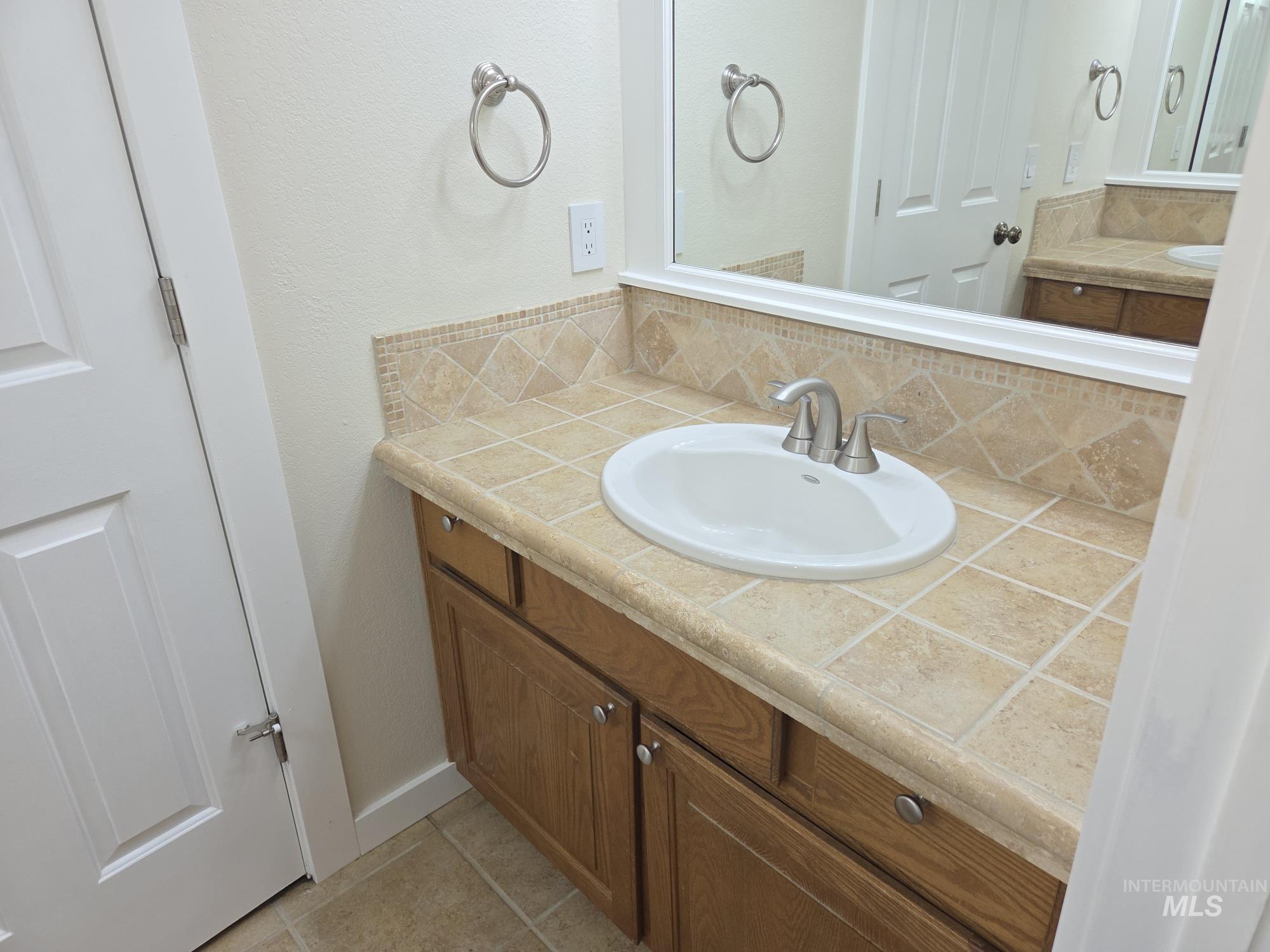 Bathroom with vanity, light tile patterned floors, a textured wall, and decorative backsplash