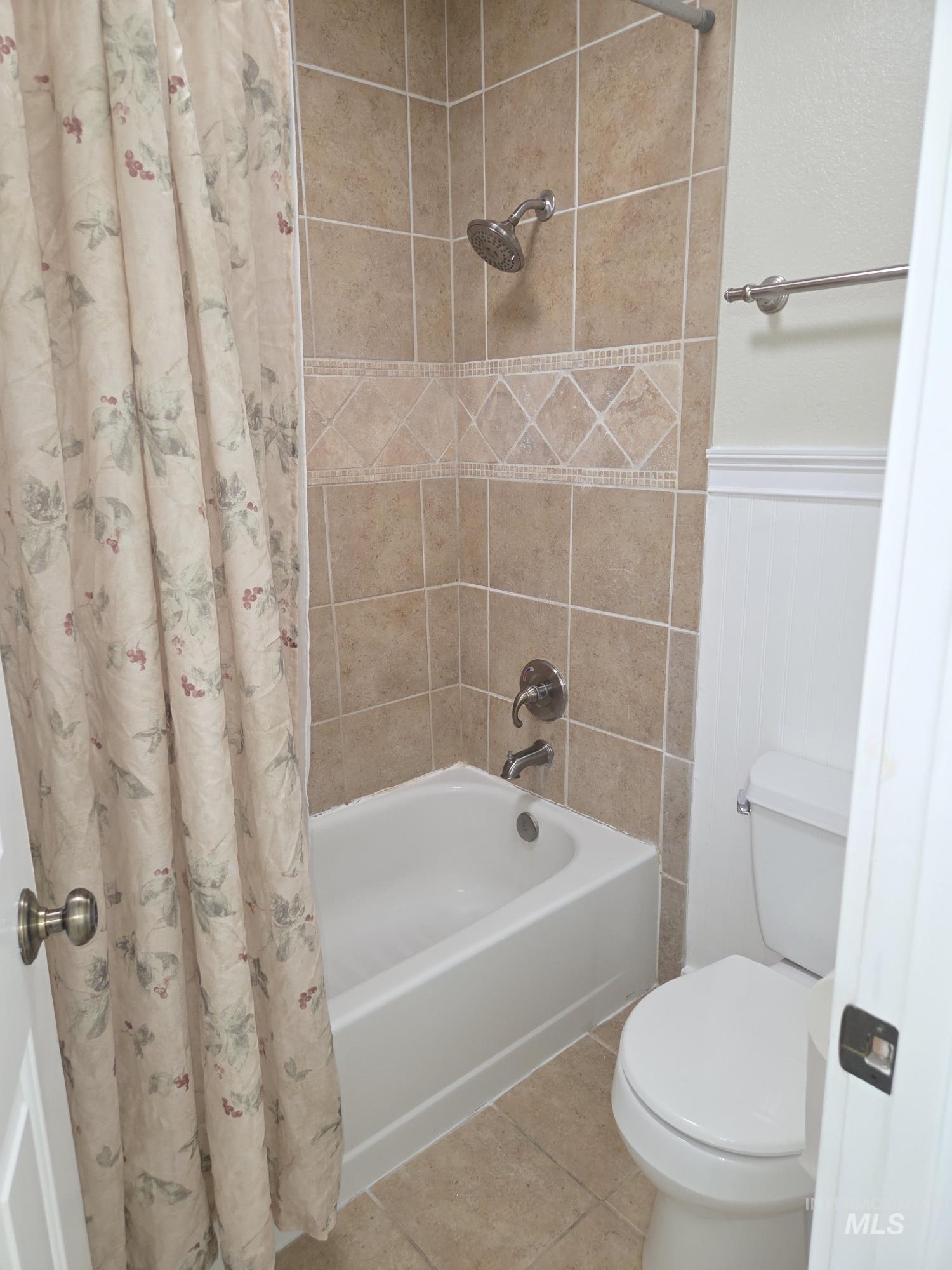 Full bathroom with tile patterned flooring, shower / bath combo with shower curtain, and wainscoting