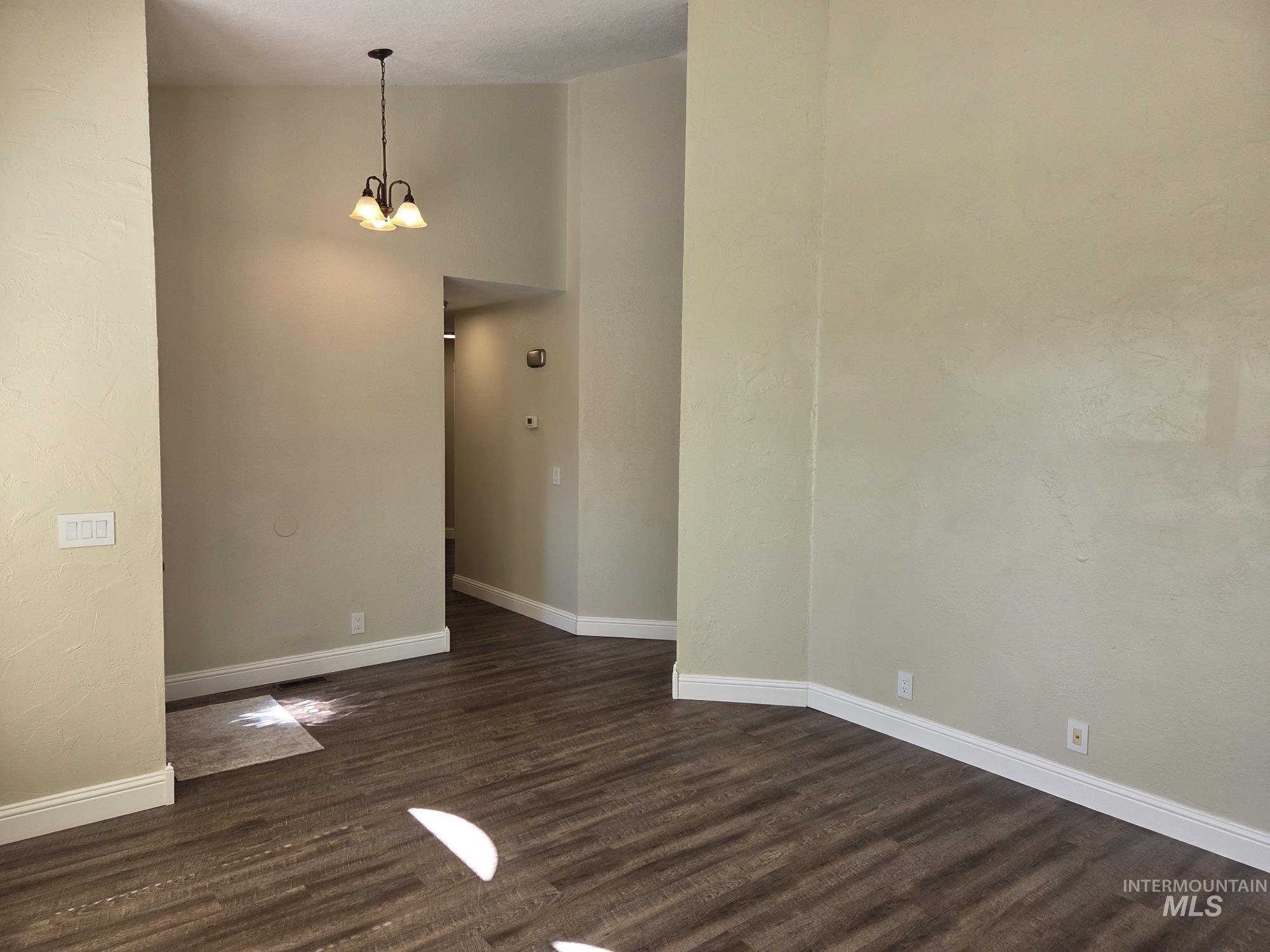Empty room featuring dark wood-type flooring, a chandelier, a high ceiling, and a textured wall