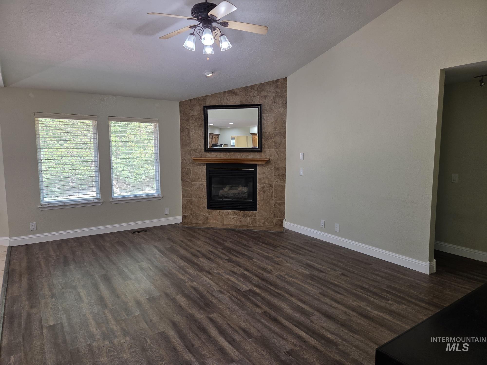 Unfurnished living room with lofted ceiling, dark wood-type flooring, a tile fireplace, a textured ceiling, and ceiling fan