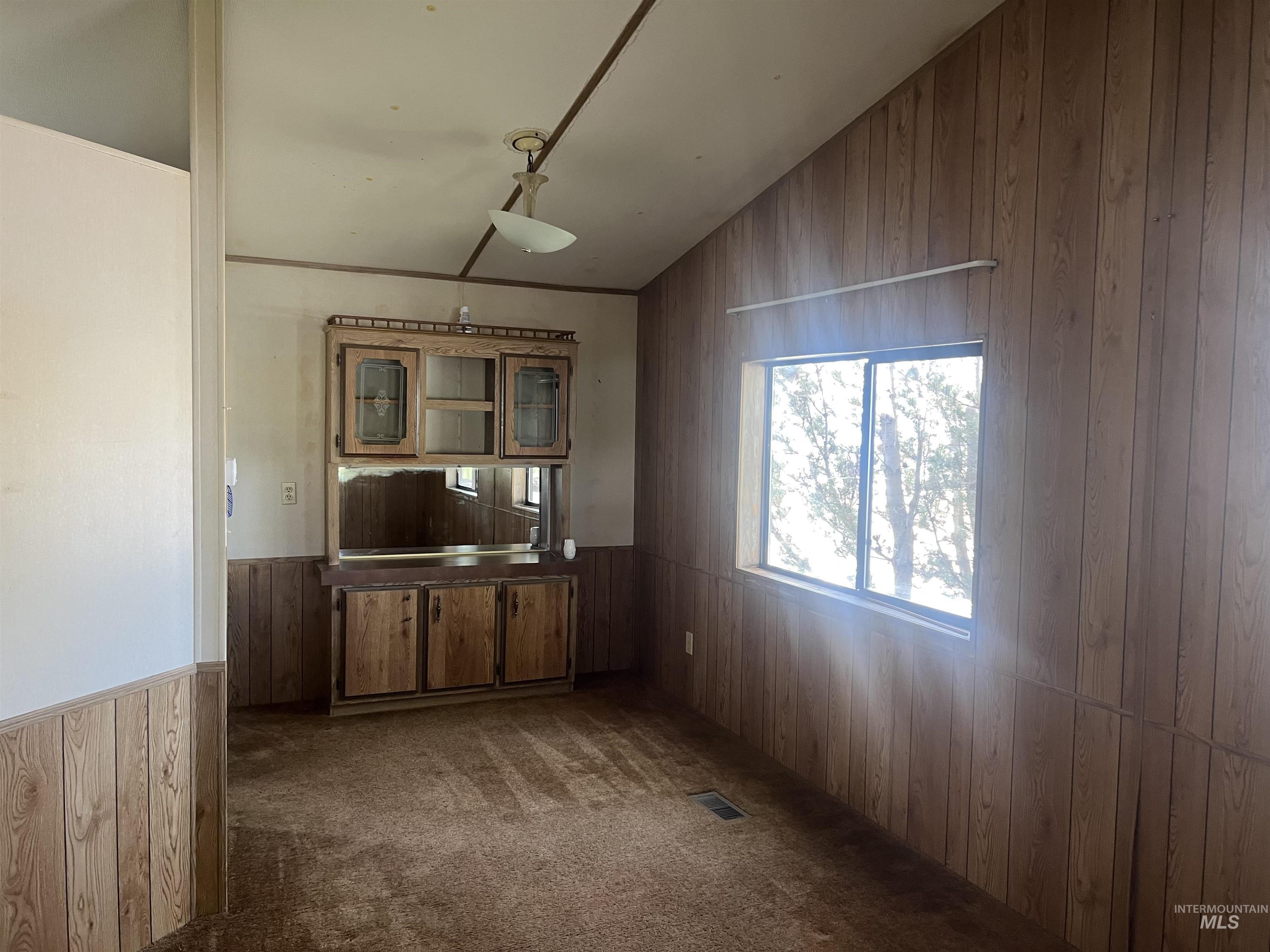 Unfurnished dining area with wooden walls, a wainscoted wall, dark carpet, and lofted ceiling