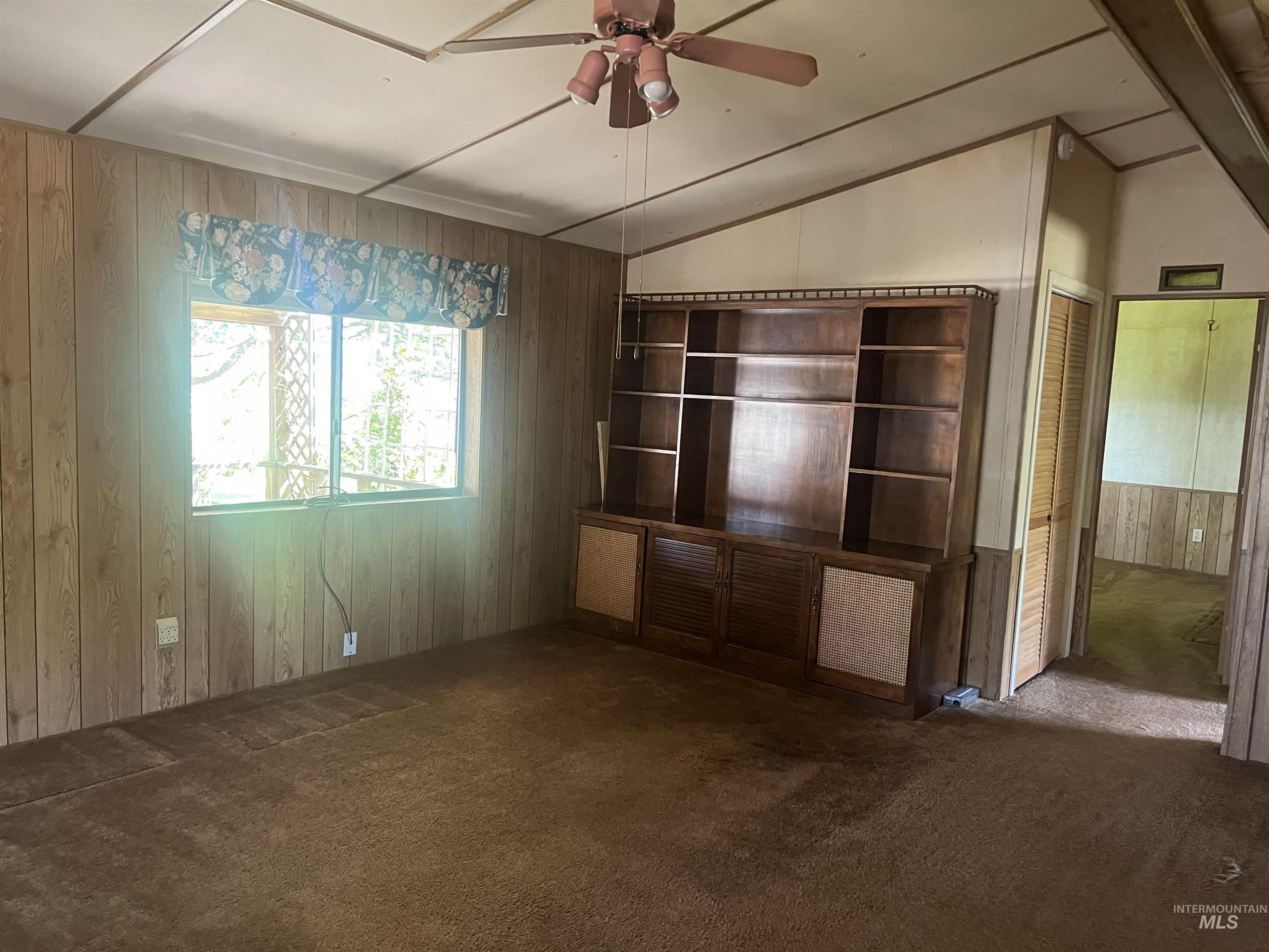 Unfurnished living room with wood walls, carpet, lofted ceiling, and ceiling fan