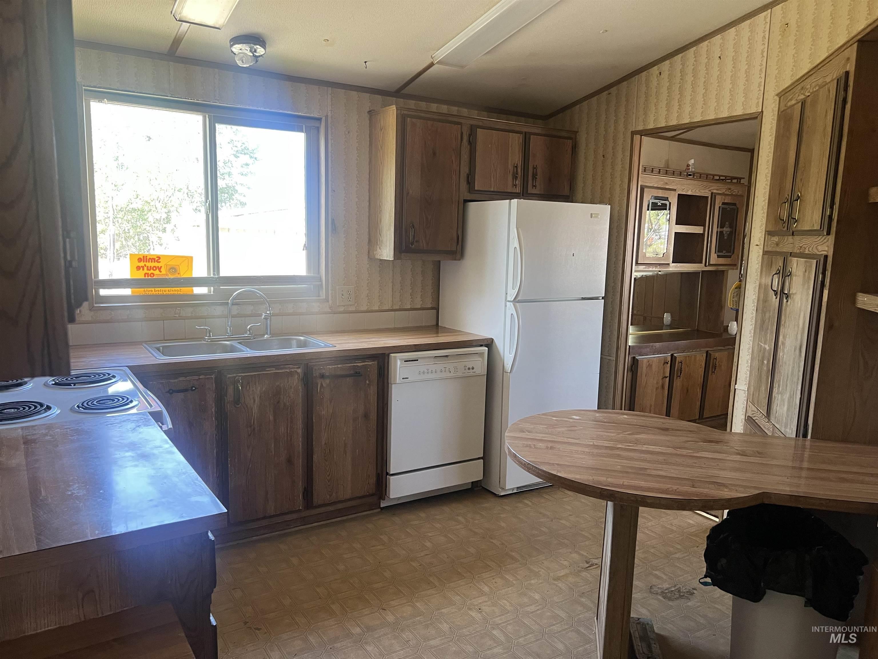 Kitchen featuring wallpapered walls, dark brown cabinetry, white appliances, light flooring, and light countertops
