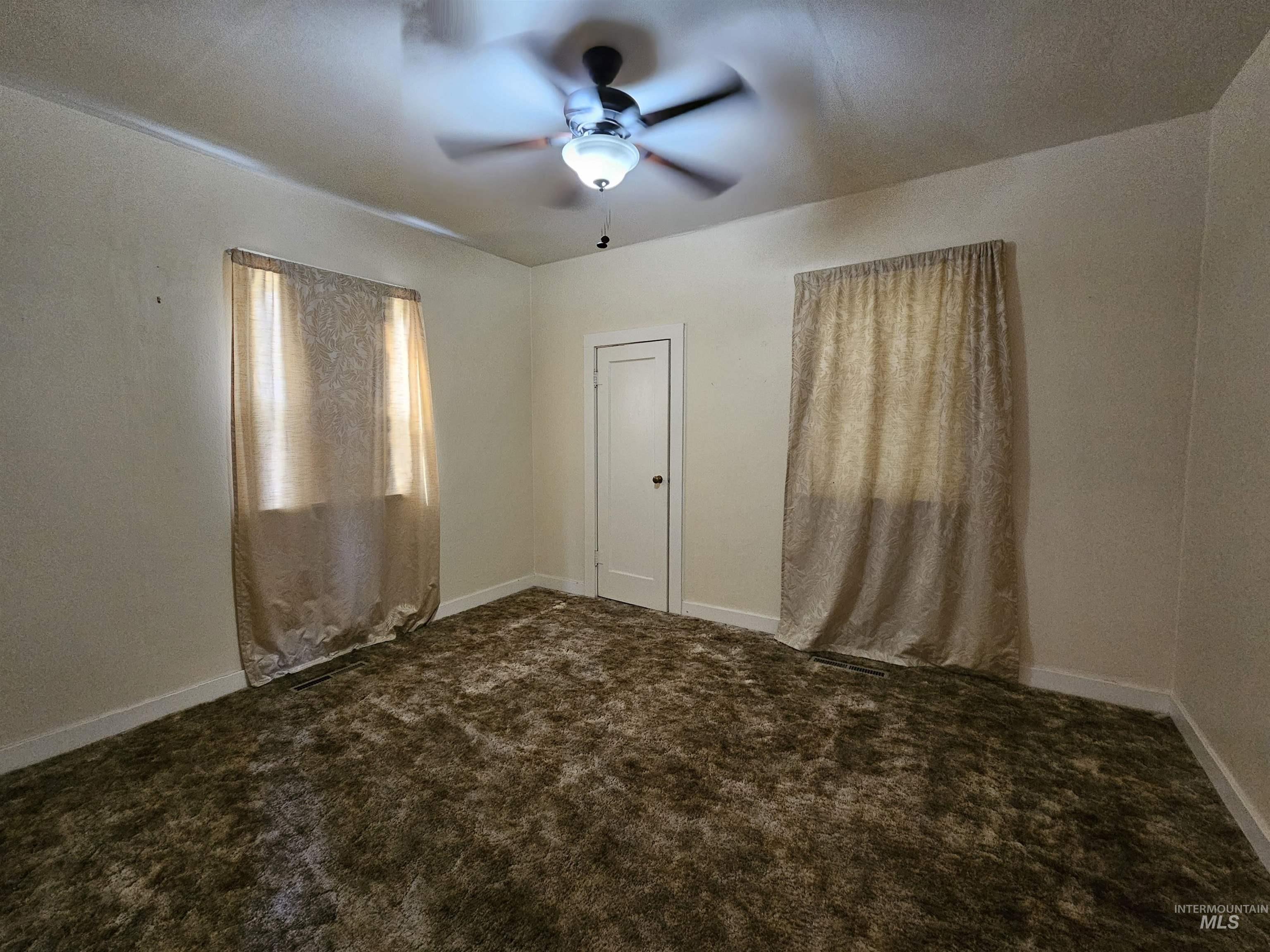 Unfurnished room featuring dark colored carpet and a ceiling fan