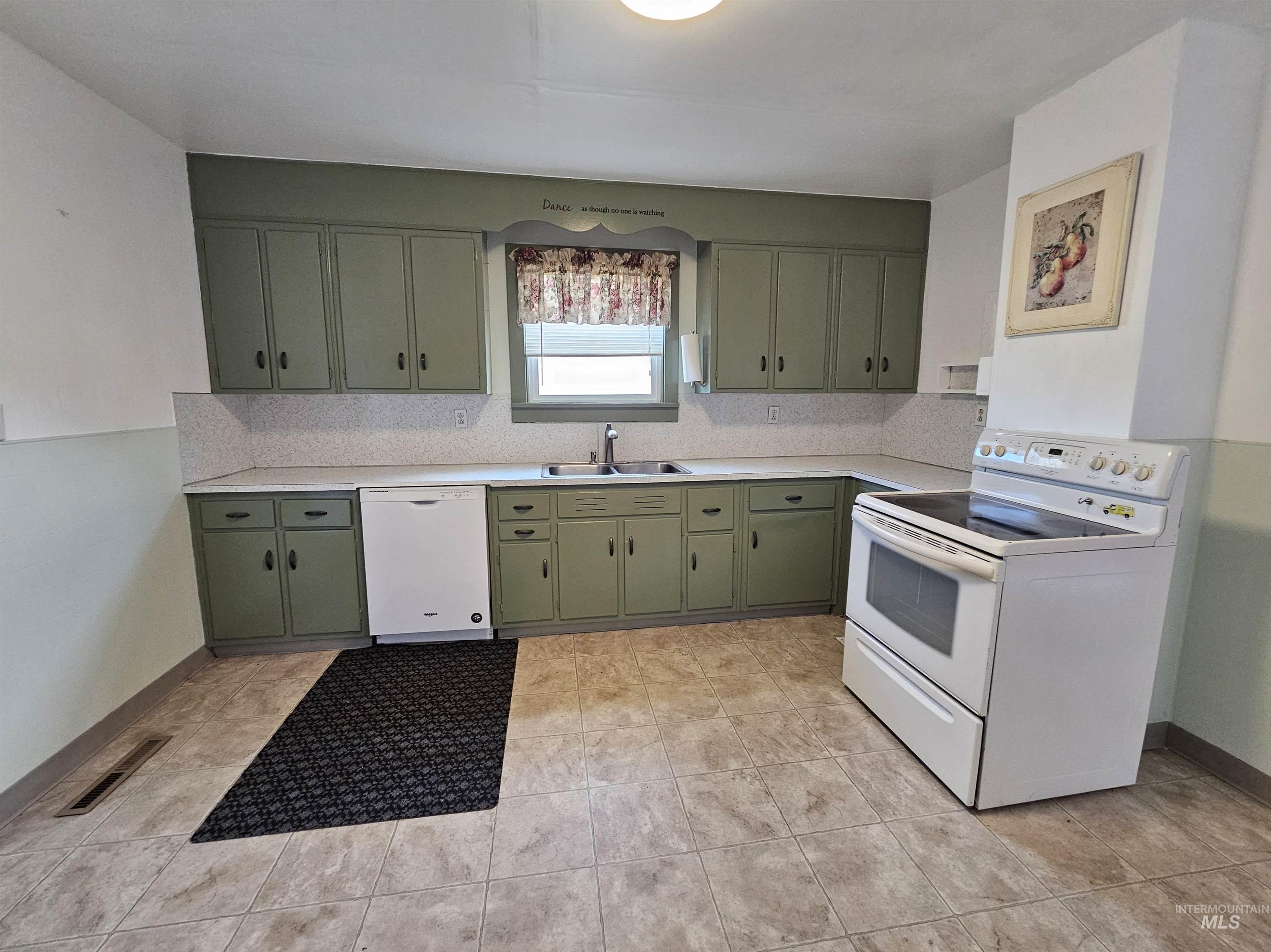 Kitchen with light countertops, white appliances, green cabinets, and tasteful backsplash