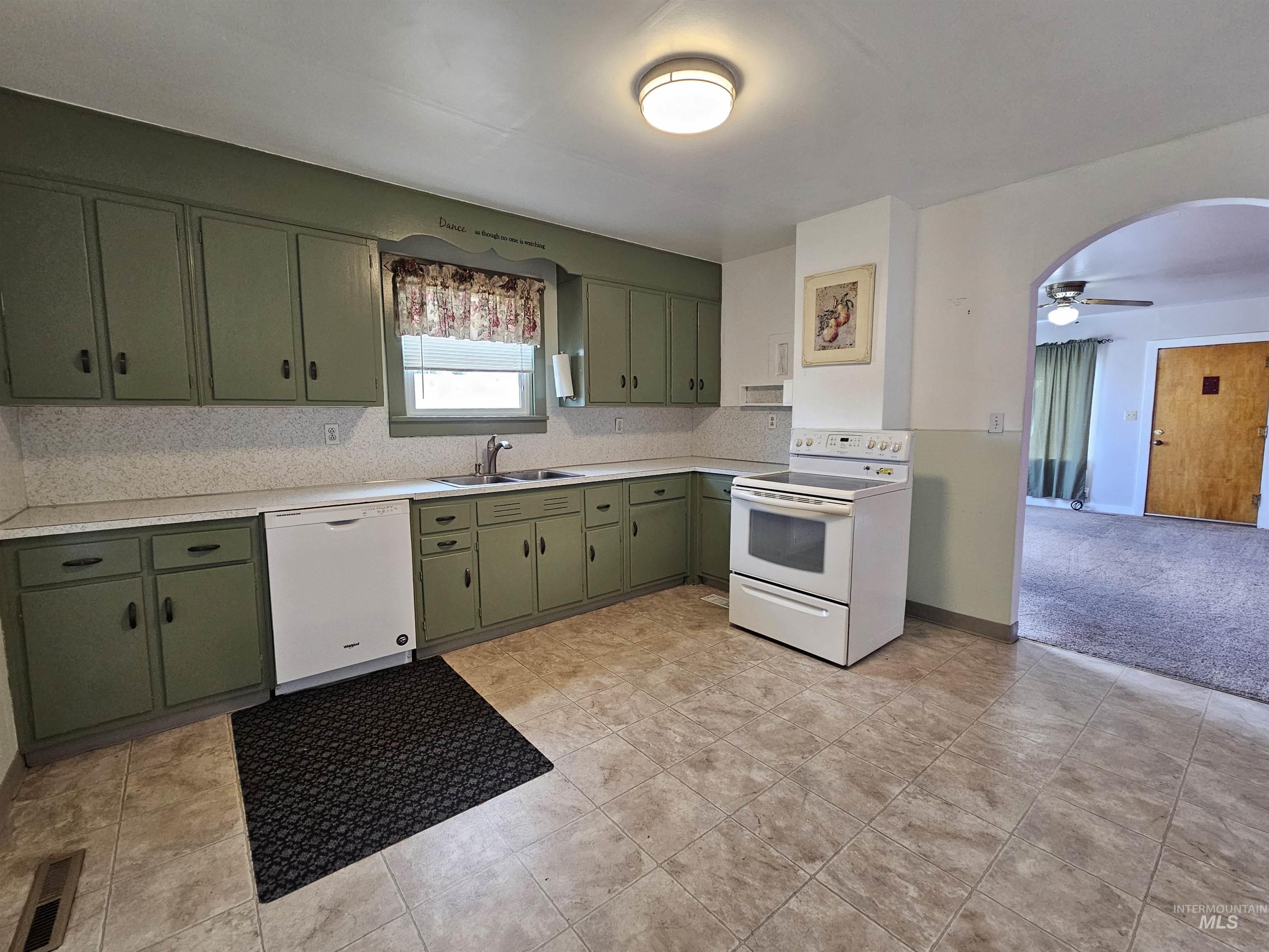Kitchen featuring green cabinetry, light countertops, white appliances, and arched walkways