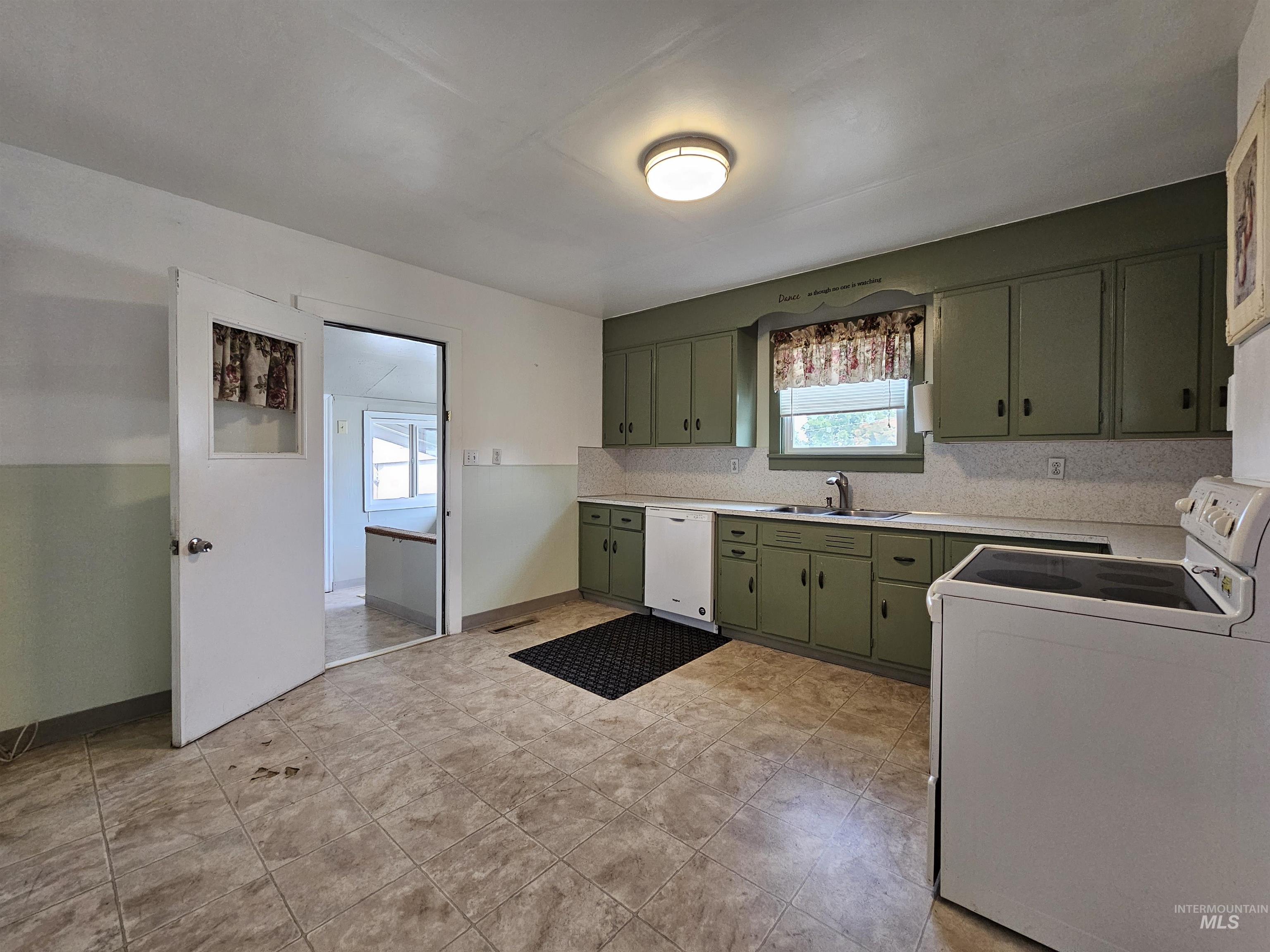 Kitchen with green cabinetry, white appliances, light countertops, and tasteful backsplash