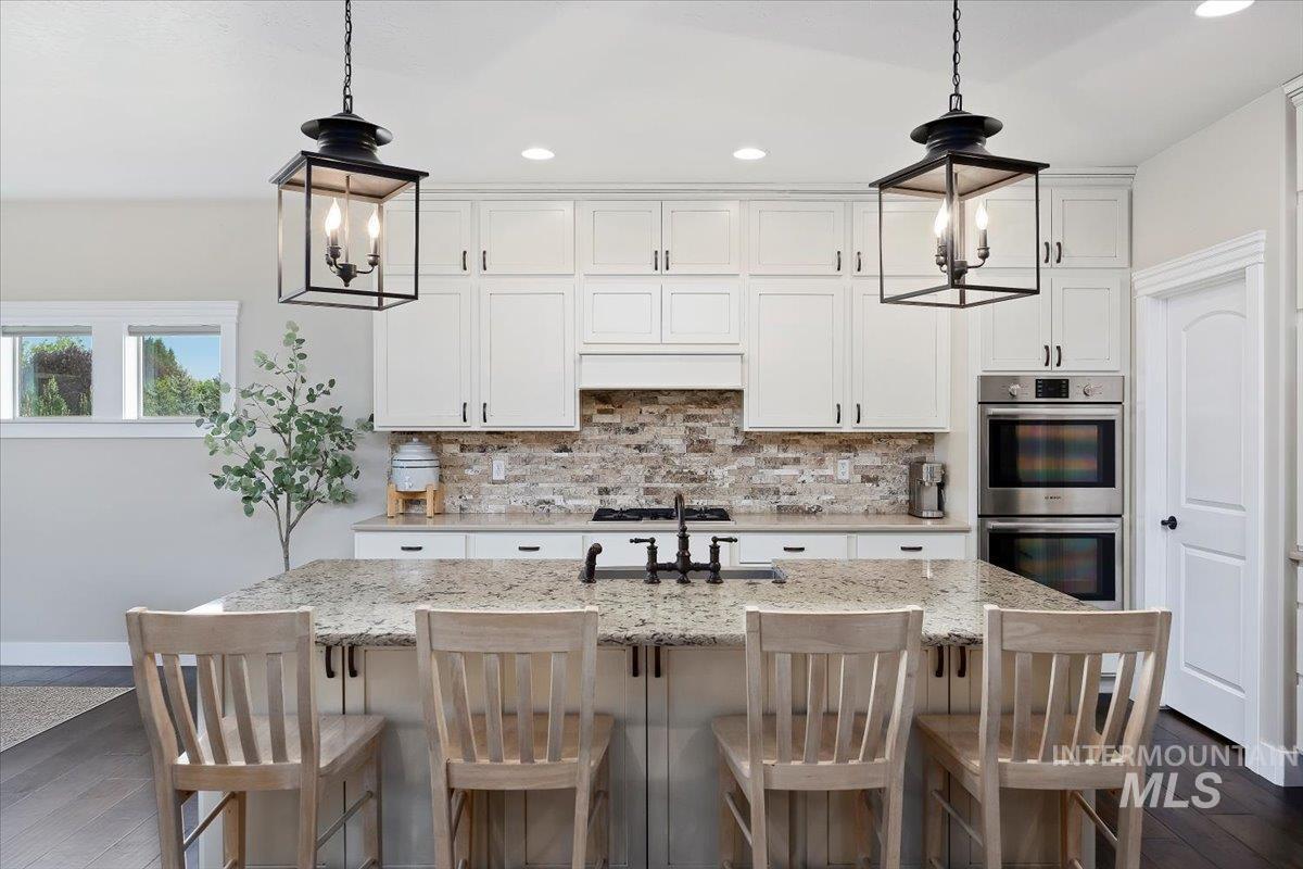 Kitchen featuring backsplash, a chandelier, dark wood-style floors, a center island with sink, and recessed lighting