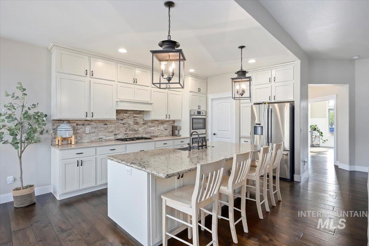 Kitchen featuring a breakfast bar area, stainless steel appliances, decorative backsplash, decorative light fixtures, and light stone countertops