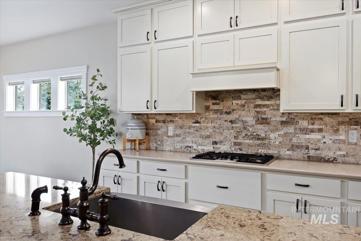 Kitchen with white cabinets, tasteful backsplash, light stone counters, stainless steel gas stovetop, and premium range hood