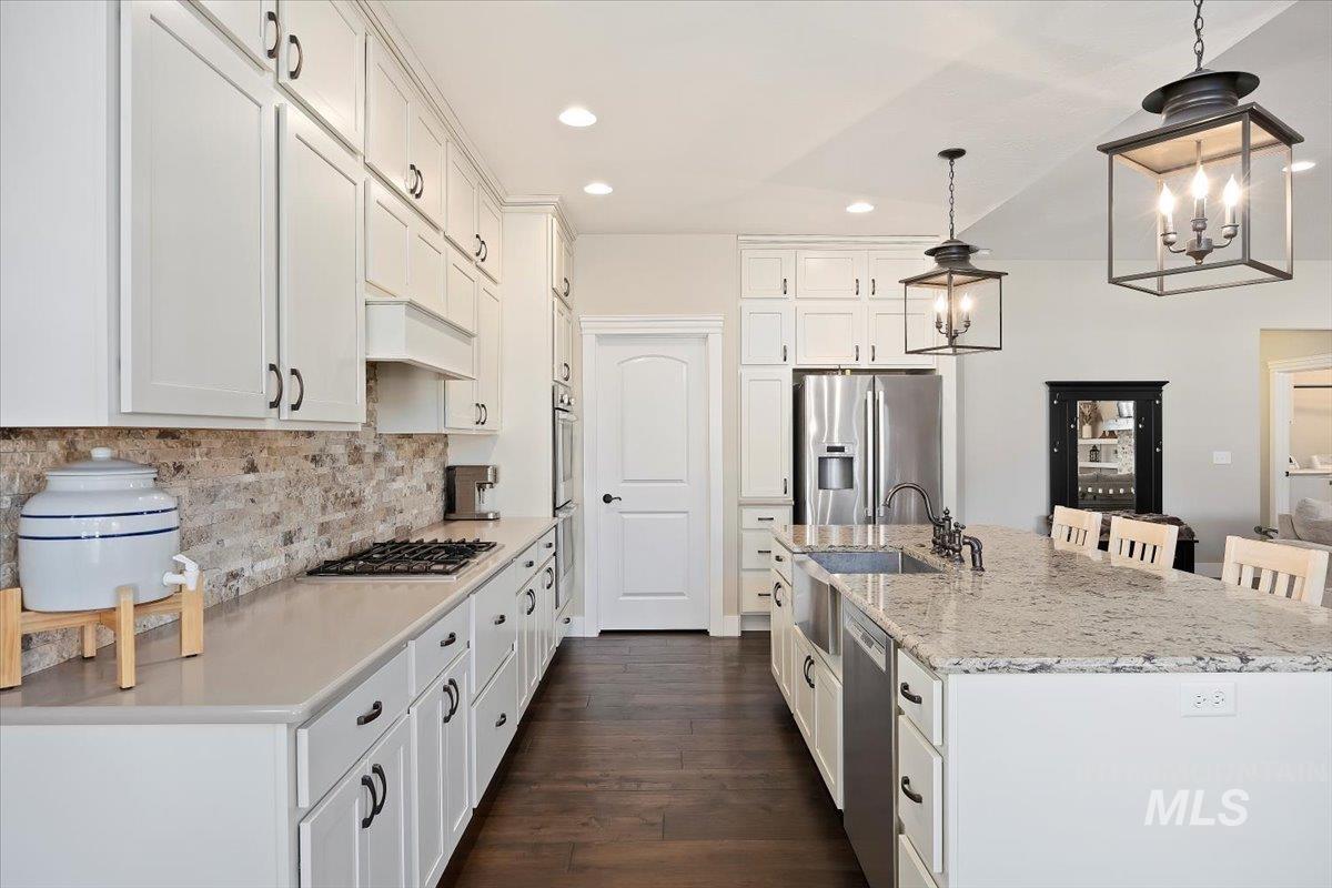 Kitchen with hanging light fixtures, recessed lighting, white cabinetry, appliances with stainless steel finishes, and a kitchen bar