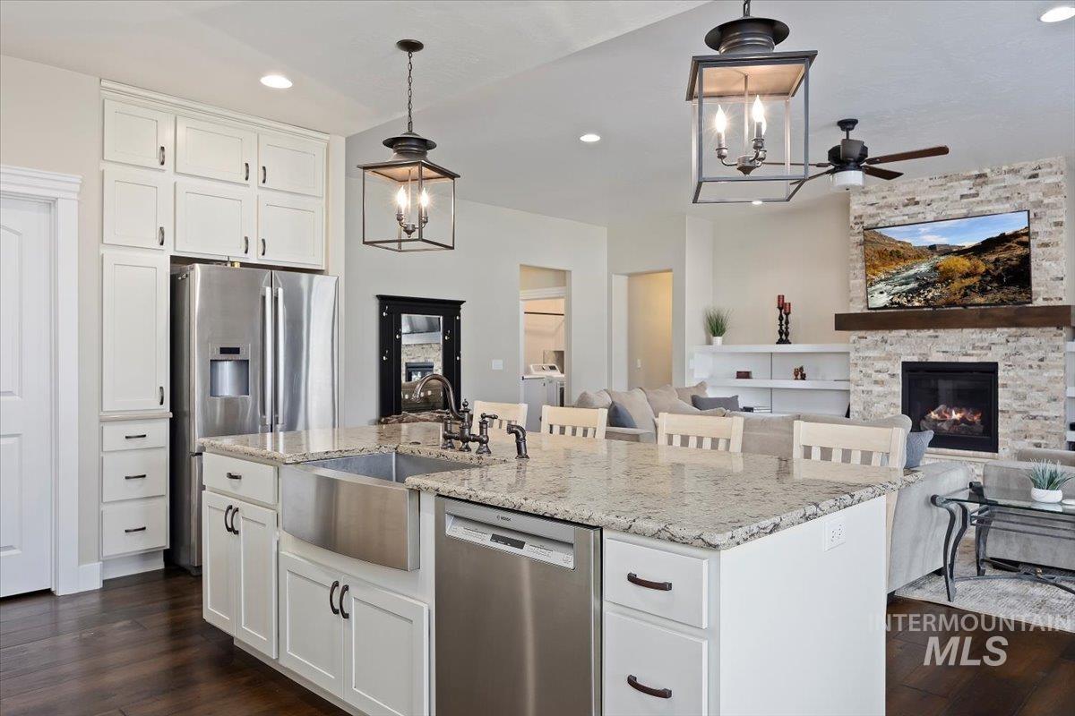 Kitchen featuring white cabinets, stainless steel appliances, light stone countertops, hanging light fixtures, and dark wood finished floors