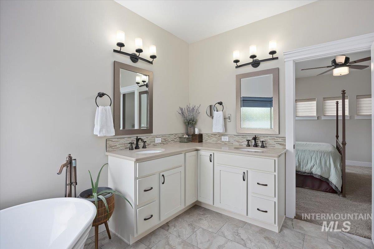 Ensuite bathroom with double vanity, a freestanding tub, tasteful backsplash, and ceiling fan
