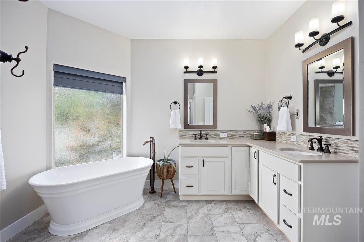 Bathroom with a soaking tub, double vanity, backsplash, and light marble finish floors