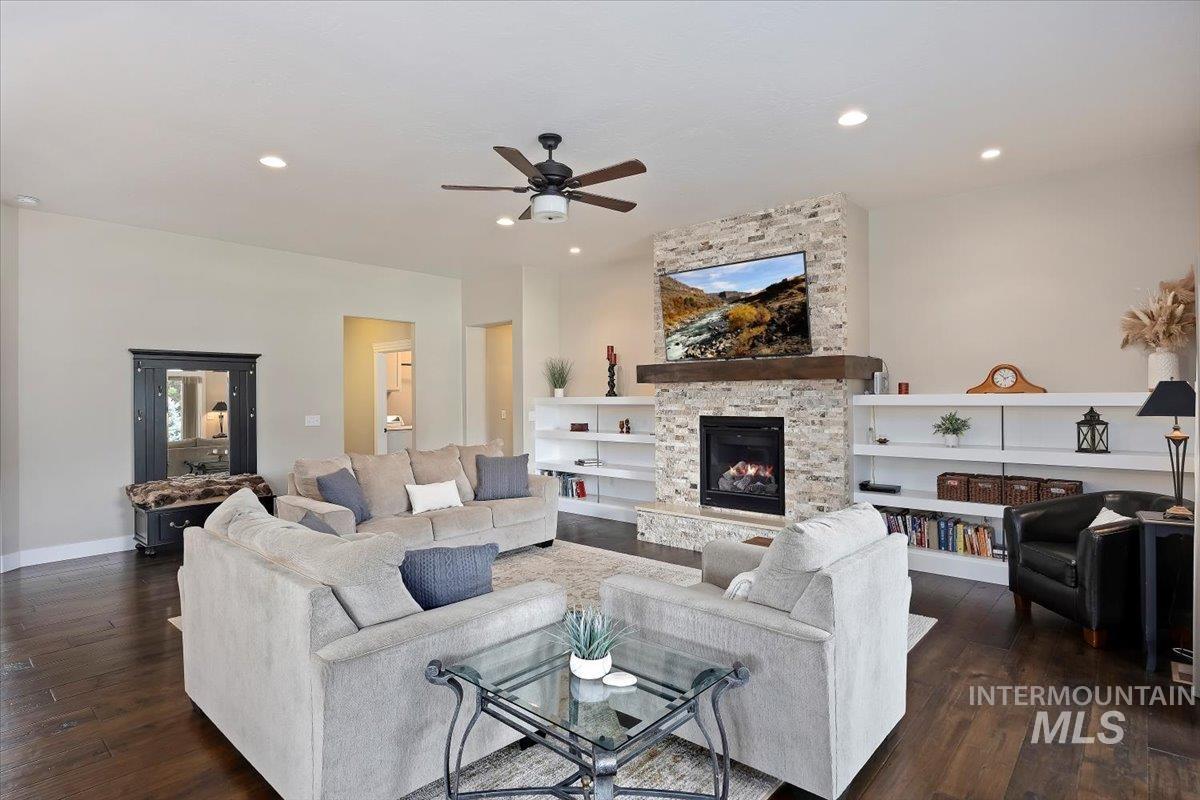 Living room featuring recessed lighting, dark wood-style floors, a stone fireplace, and a ceiling fan