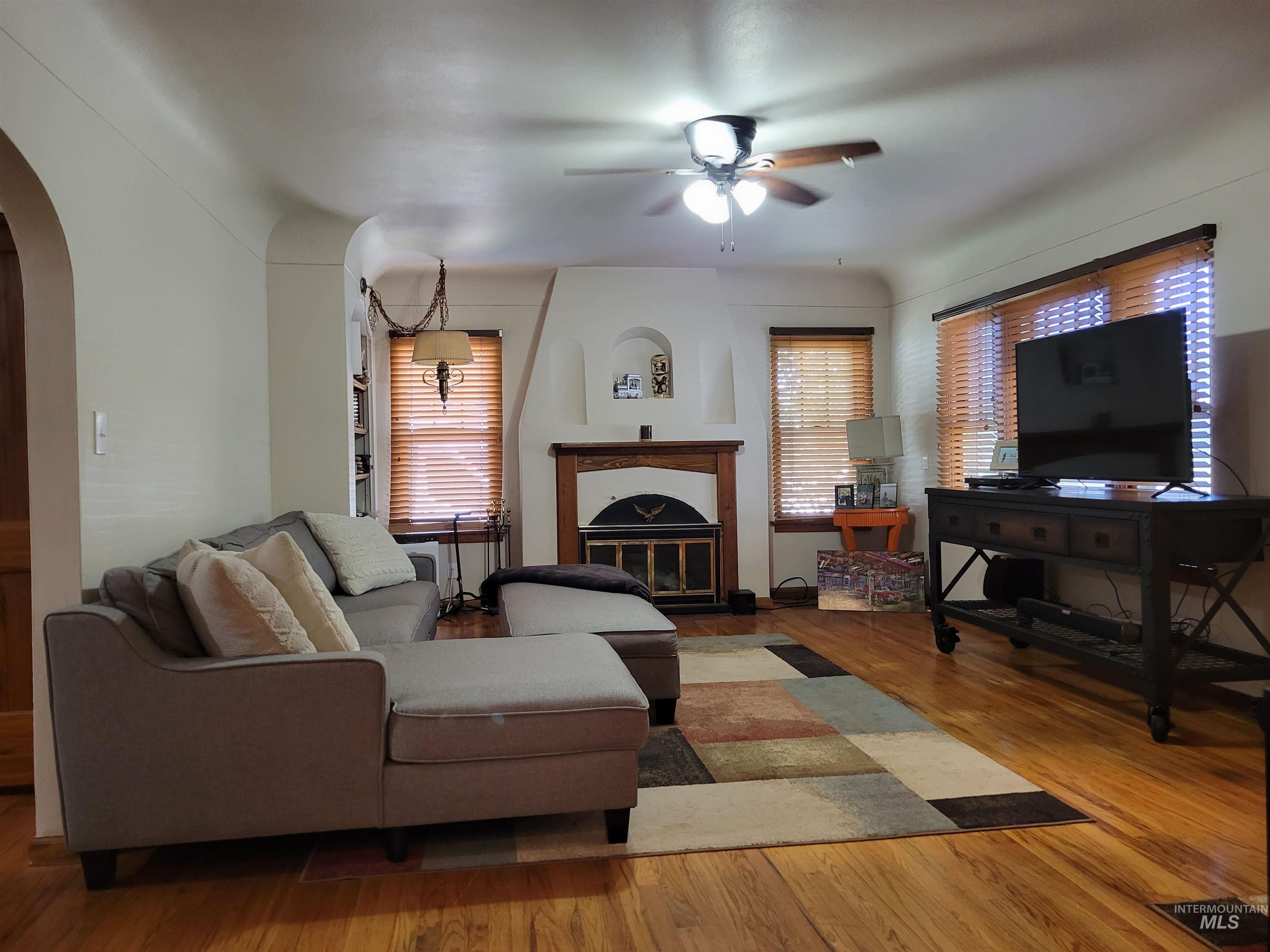 Living room featuring wood finished floors, ceiling fan, arched walkways, and a glass covered fireplace