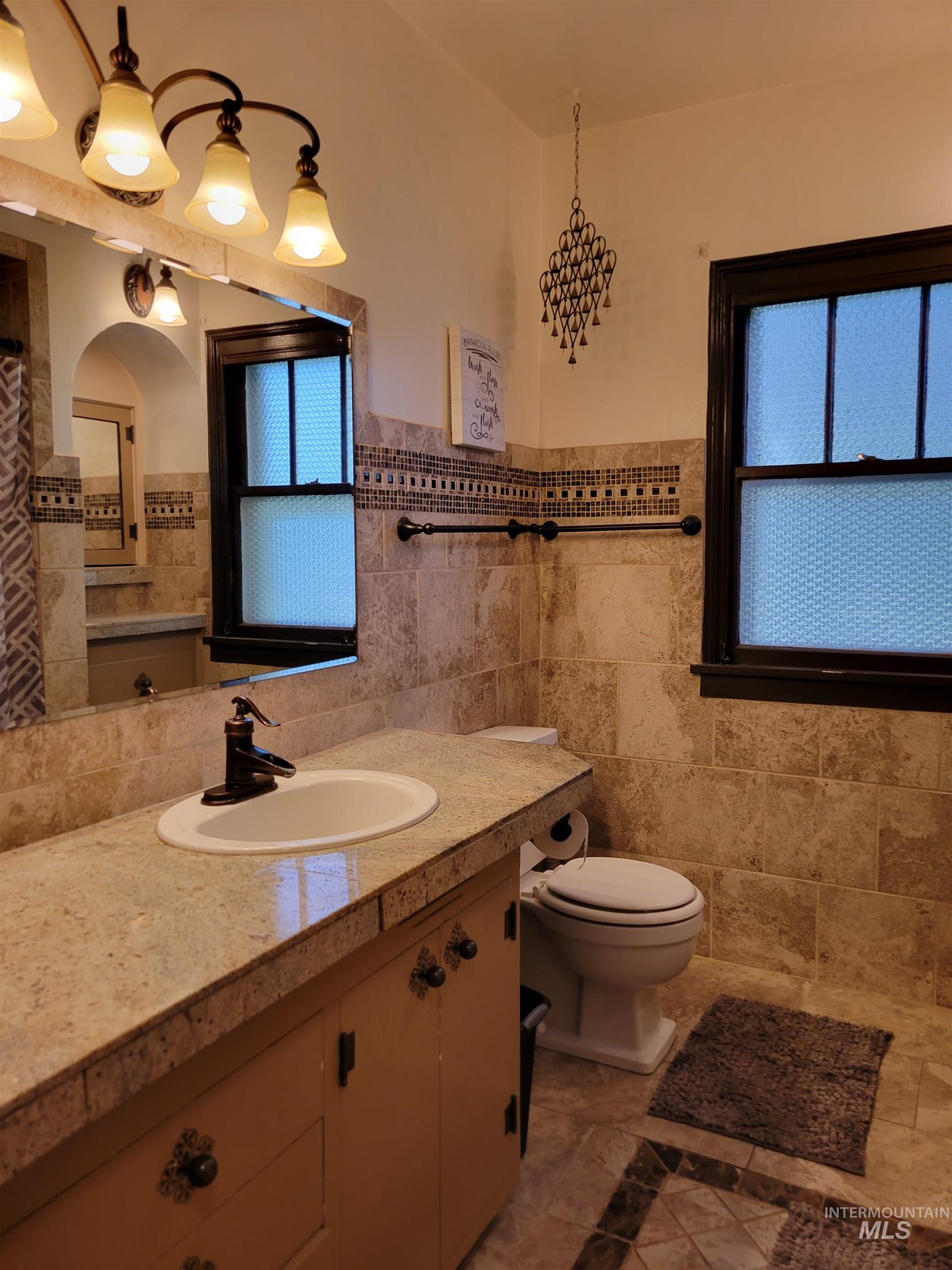 Full bath with vanity, tile walls, light tile patterned floors, and wainscoting