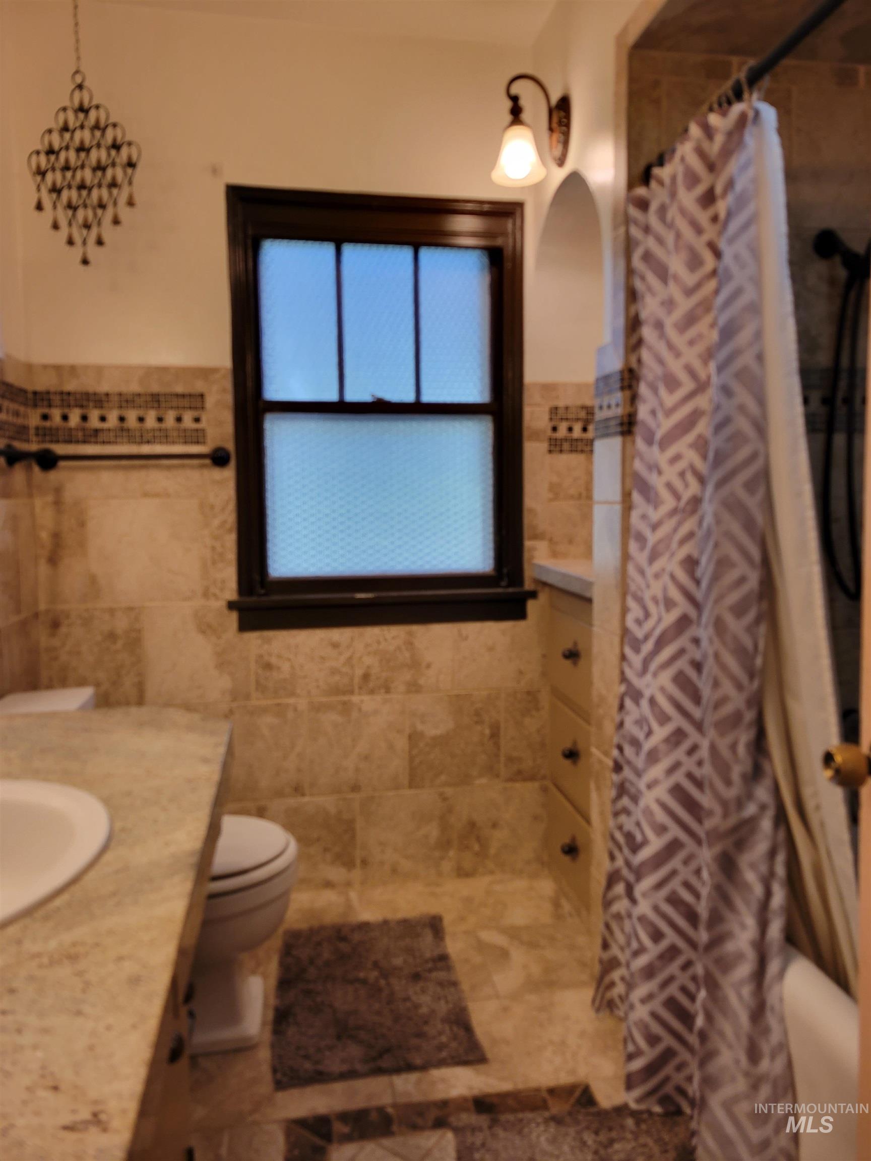 Bathroom featuring vanity, tile walls, wainscoting, shower / bathtub combination with curtain, and tile patterned flooring