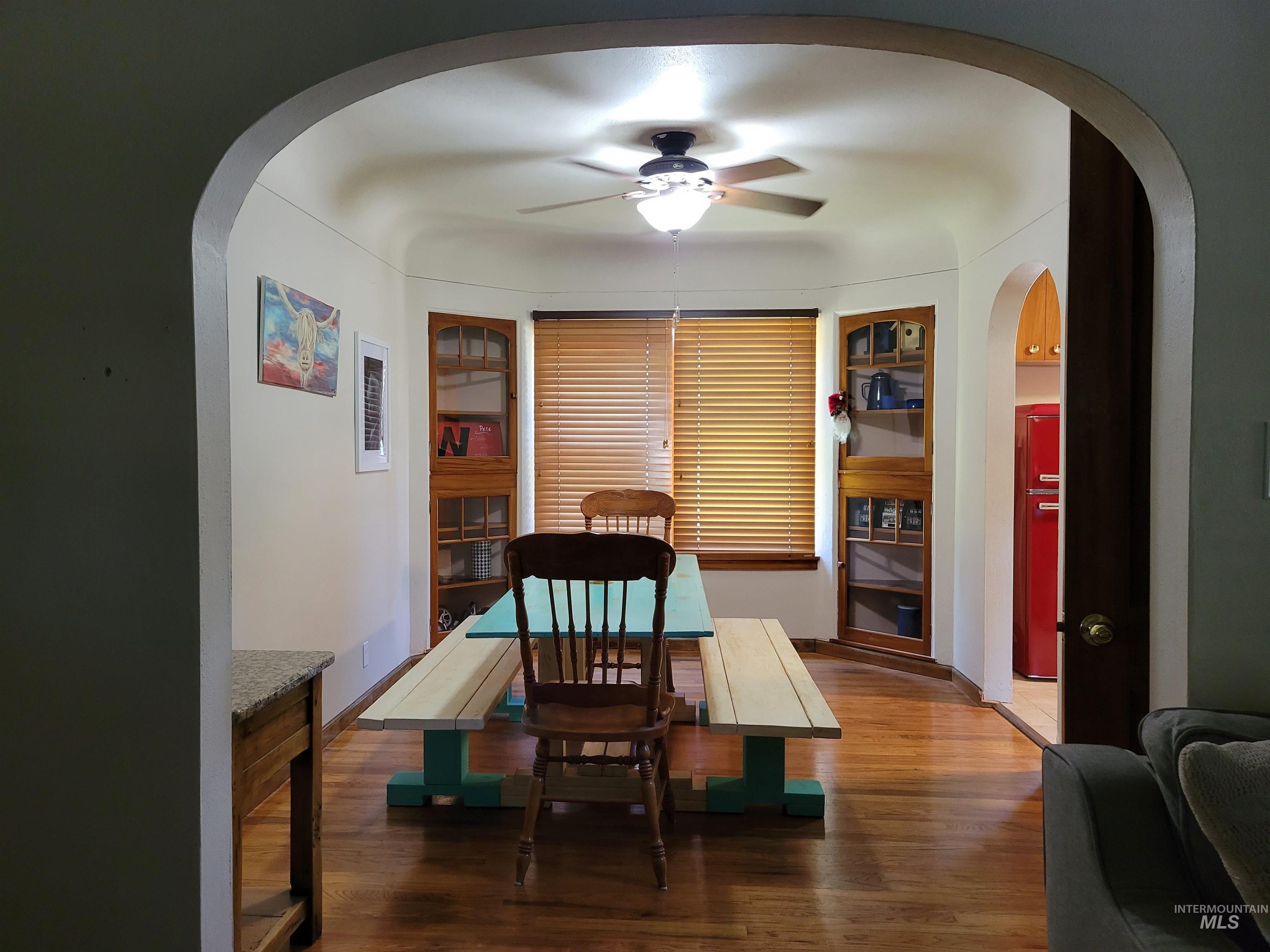 Dining space with arched walkways, wood finished floors, and ceiling fan