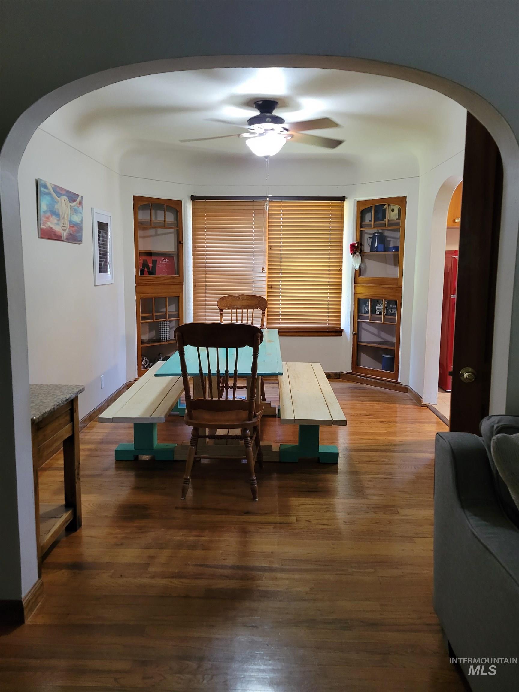 Dining space with arched walkways, dark wood finished floors, and ceiling fan
