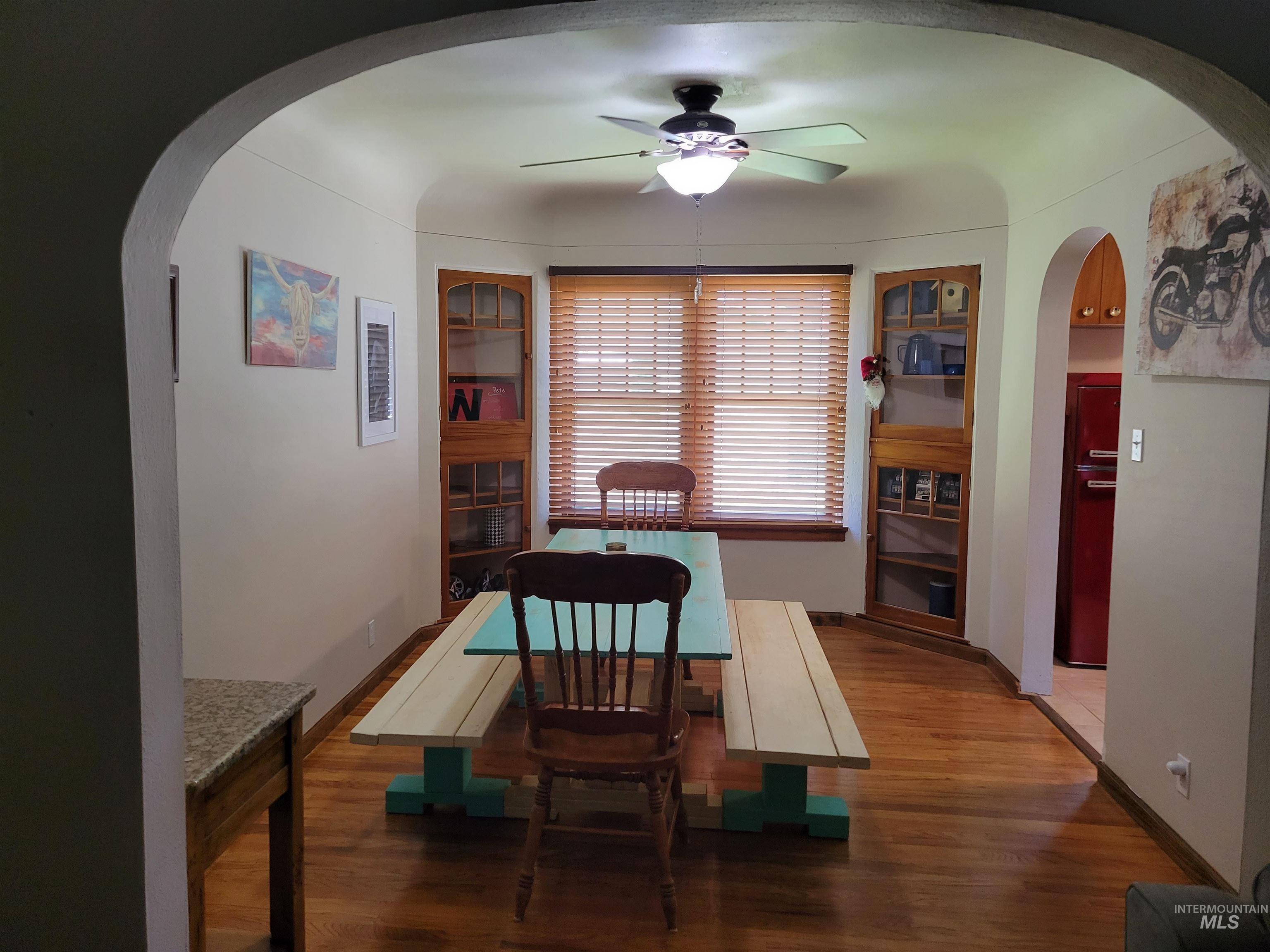 Dining room with arched walkways, wood finished floors, and a ceiling fan