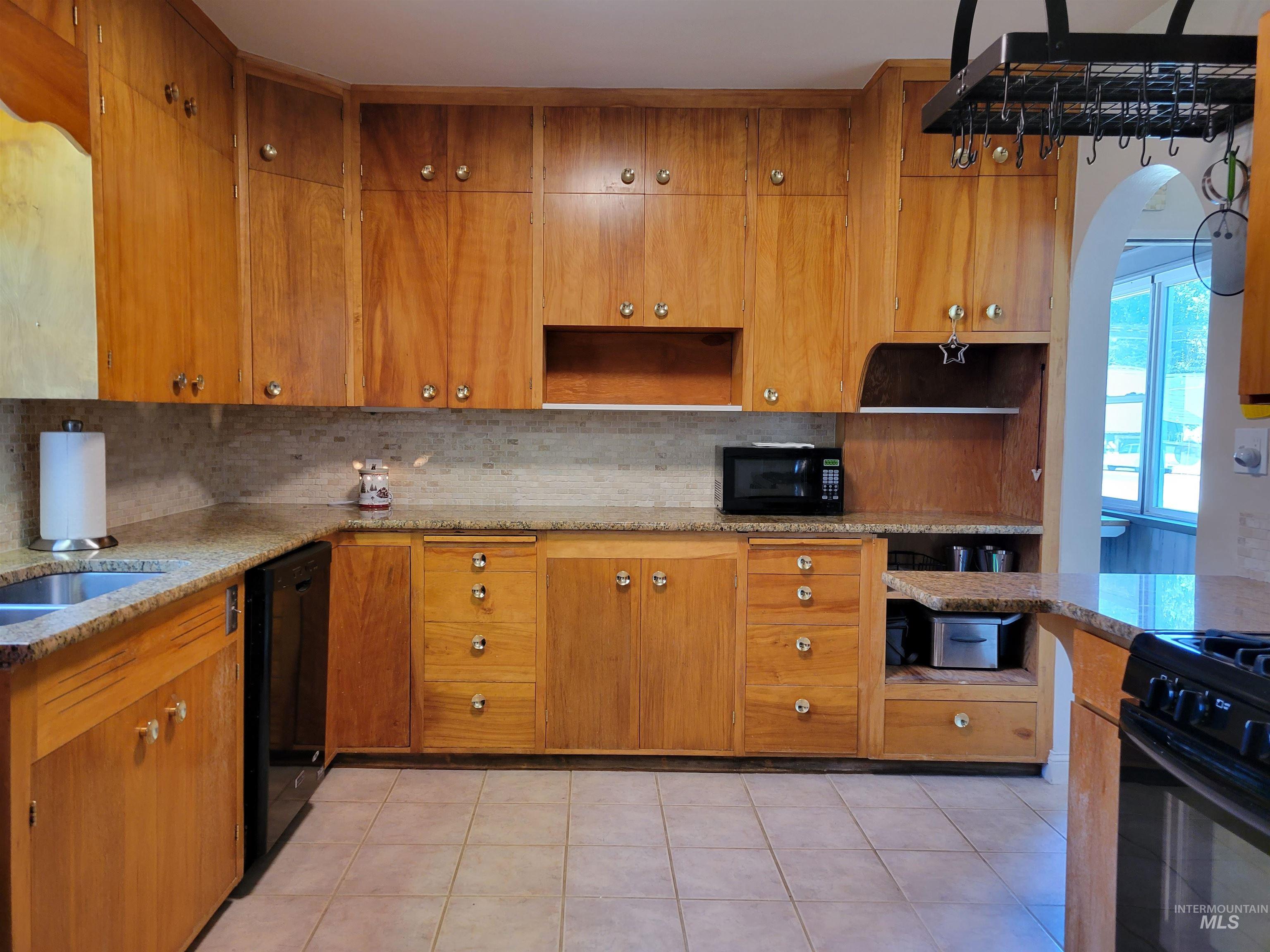 Kitchen featuring decorative backsplash, brown cabinetry, arched walkways, and light tile patterned flooring