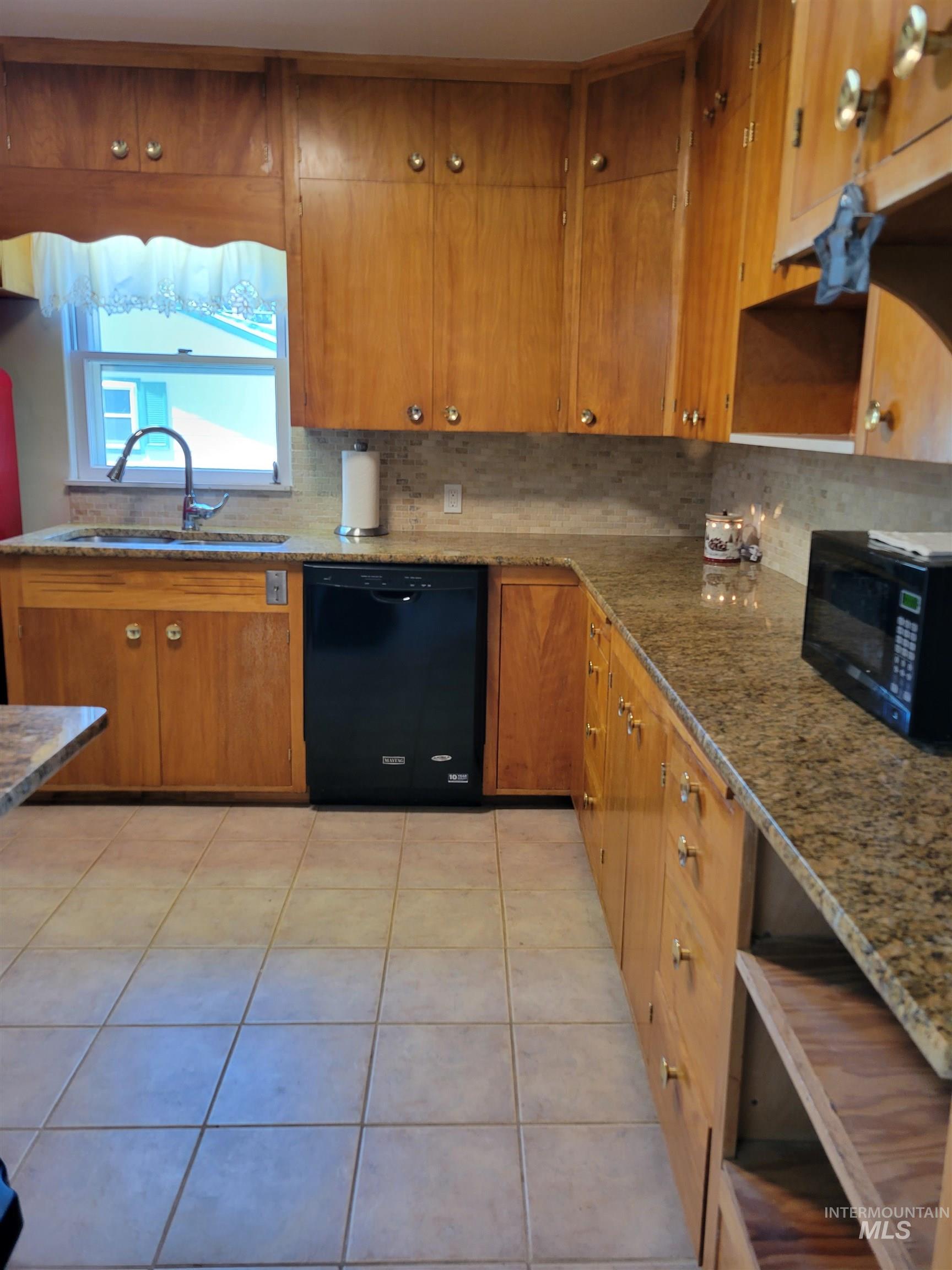Kitchen featuring brown cabinetry, black appliances, light tile patterned floors, tasteful backsplash, and open shelves