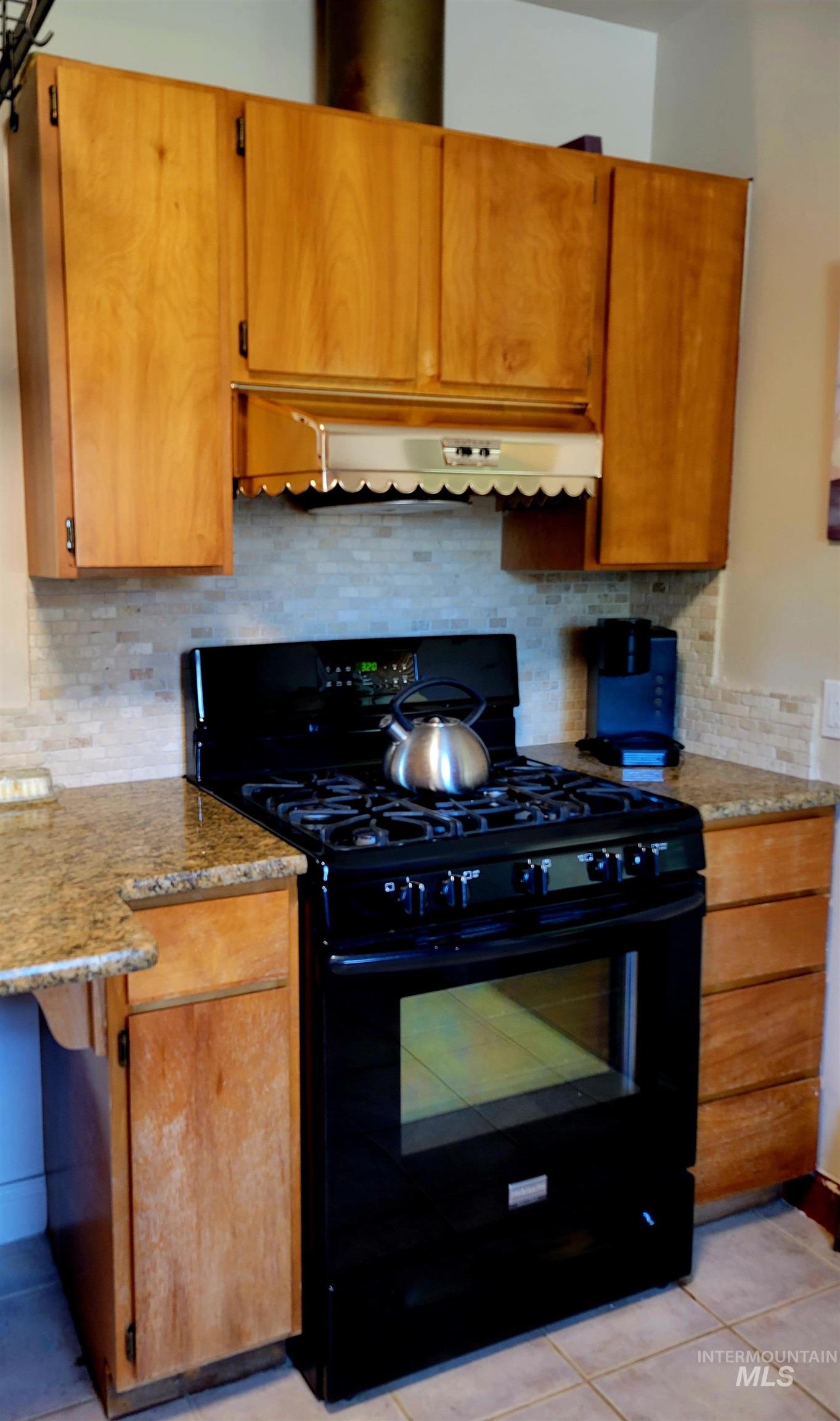 Kitchen with tasteful backsplash, black gas range, brown cabinetry, and range hood