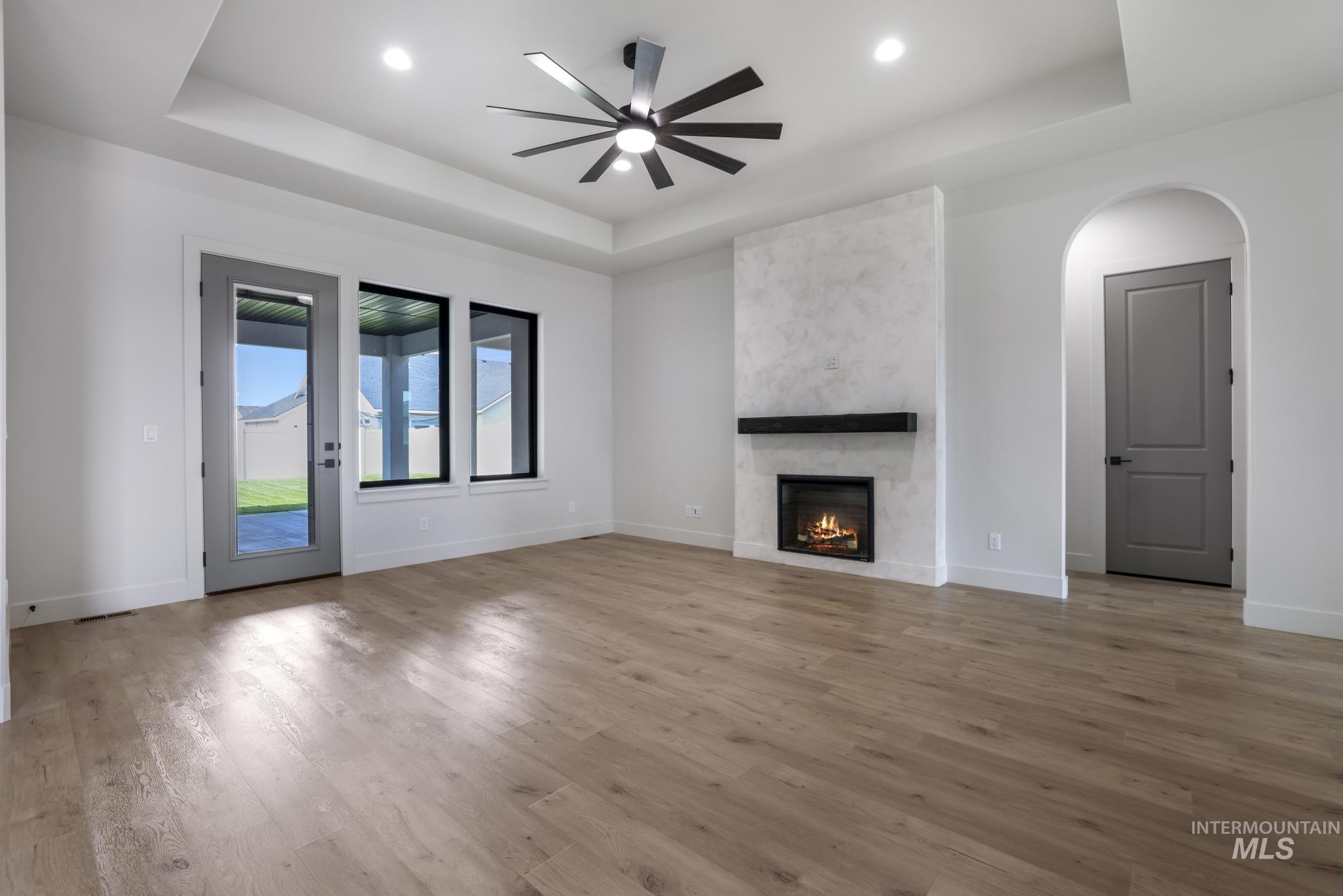 Unfurnished living room with a raised ceiling, ceiling fan, light wood finished floors, a fireplace, and recessed lighting
