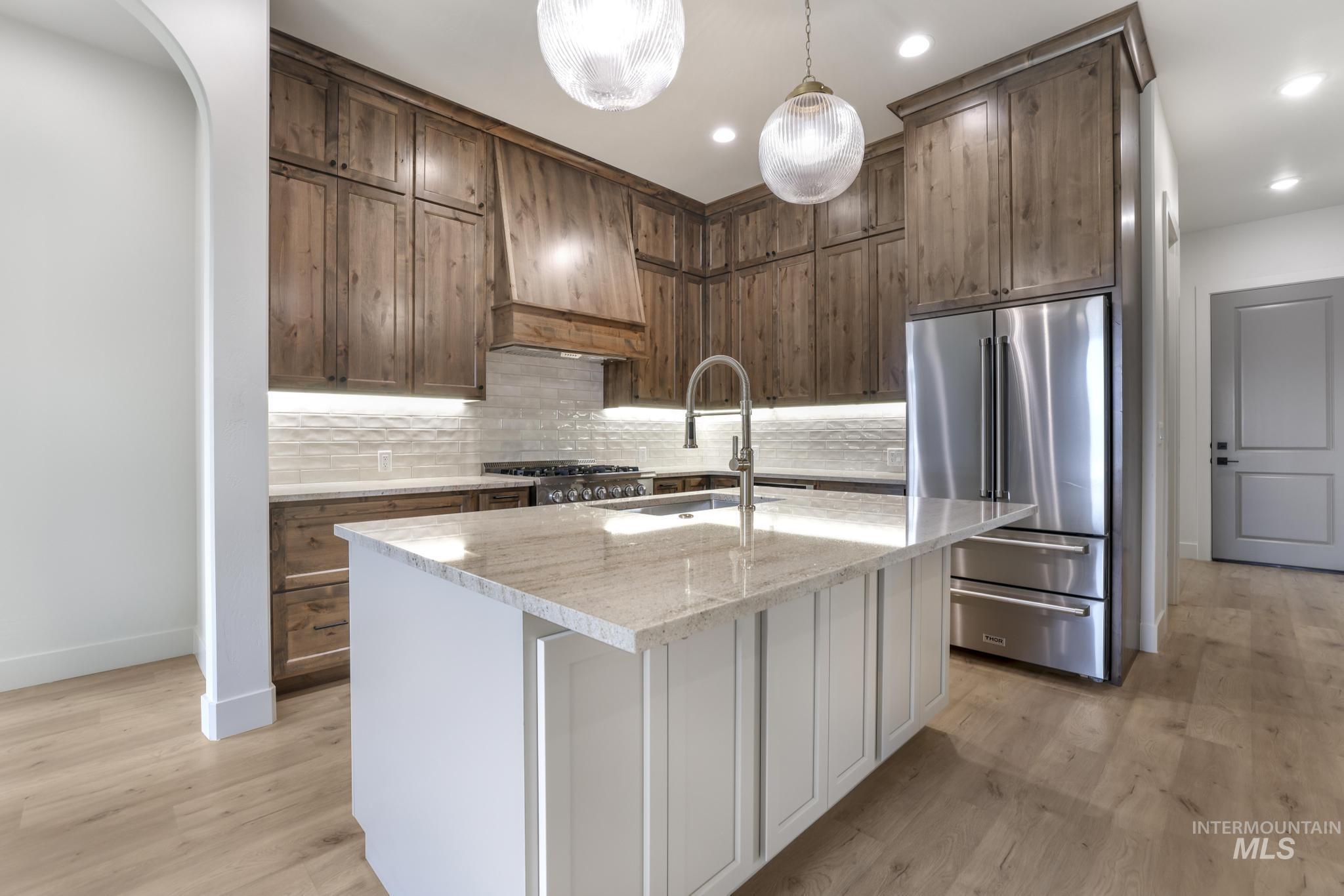 Kitchen featuring light stone counters, appliances with stainless steel finishes, backsplash, a center island with sink, and hanging light fixtures