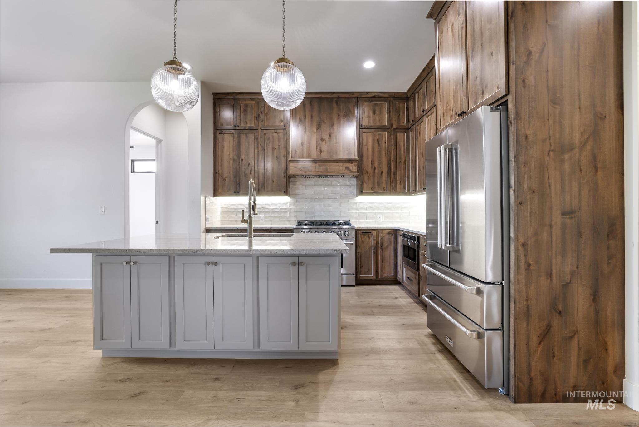 Kitchen with high end appliances, tasteful backsplash, hanging light fixtures, light stone counters, and light wood-style floors