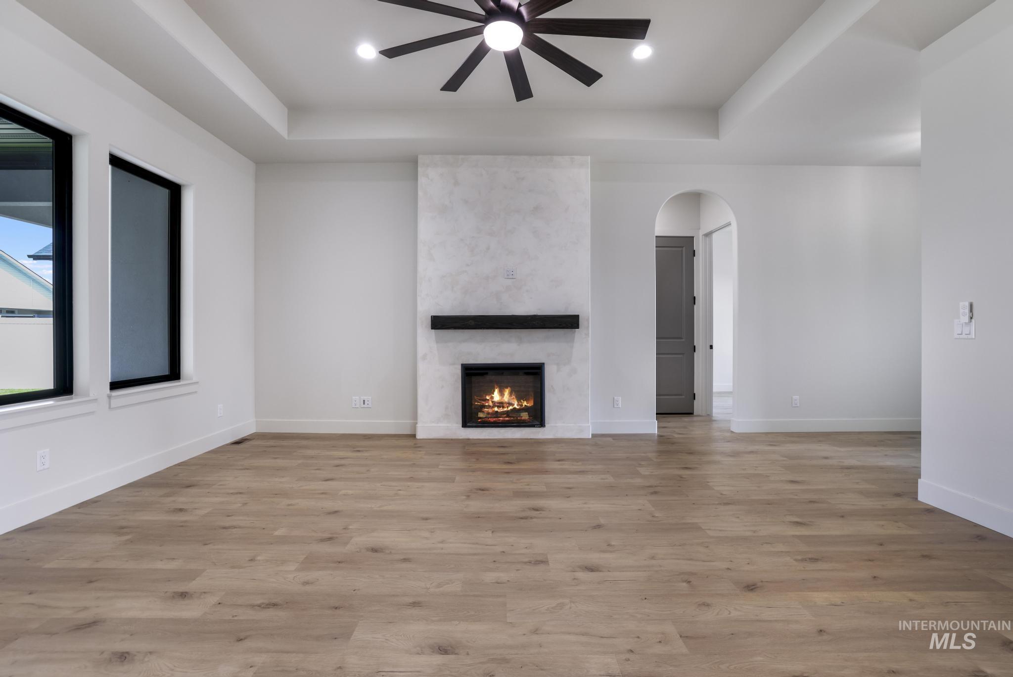 Unfurnished living room with a raised ceiling, a large fireplace, light wood finished floors, a ceiling fan, and recessed lighting