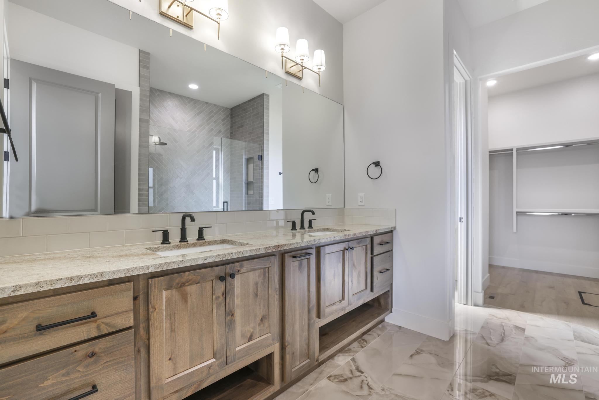 Bathroom featuring light marble finish flooring, a shower stall, double vanity, a walk in closet, and recessed lighting