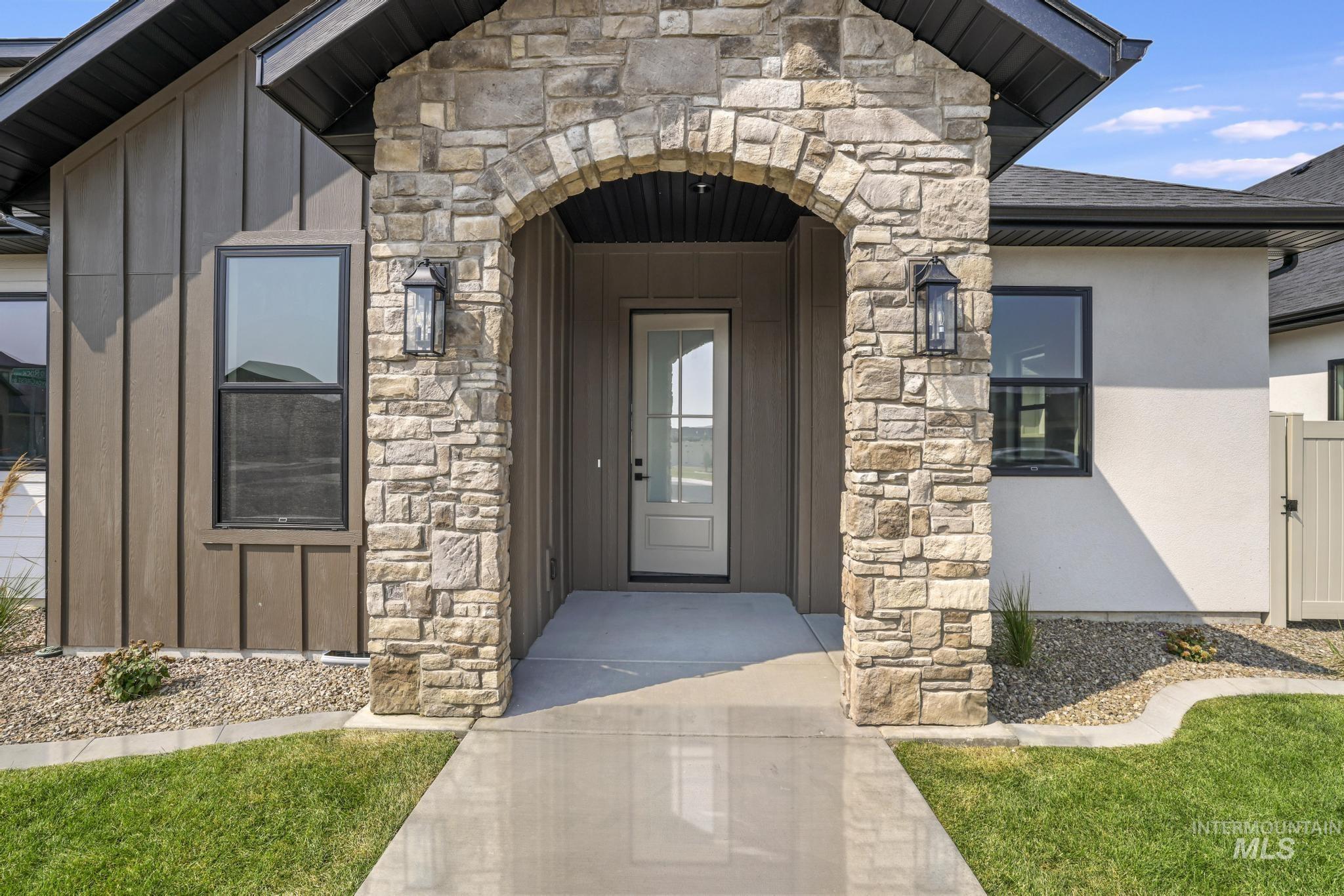View of exterior entry with stone siding, board and batten siding, a shingled roof, and stucco siding