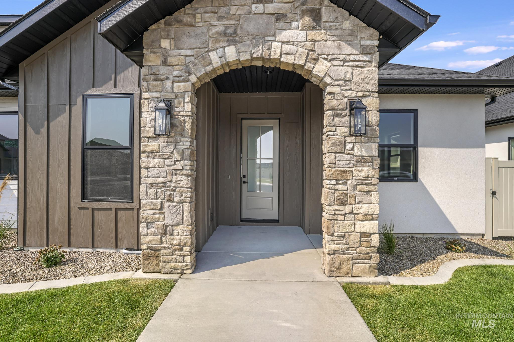 Doorway to property with stone siding, board and batten siding, roof with shingles, and stucco siding
