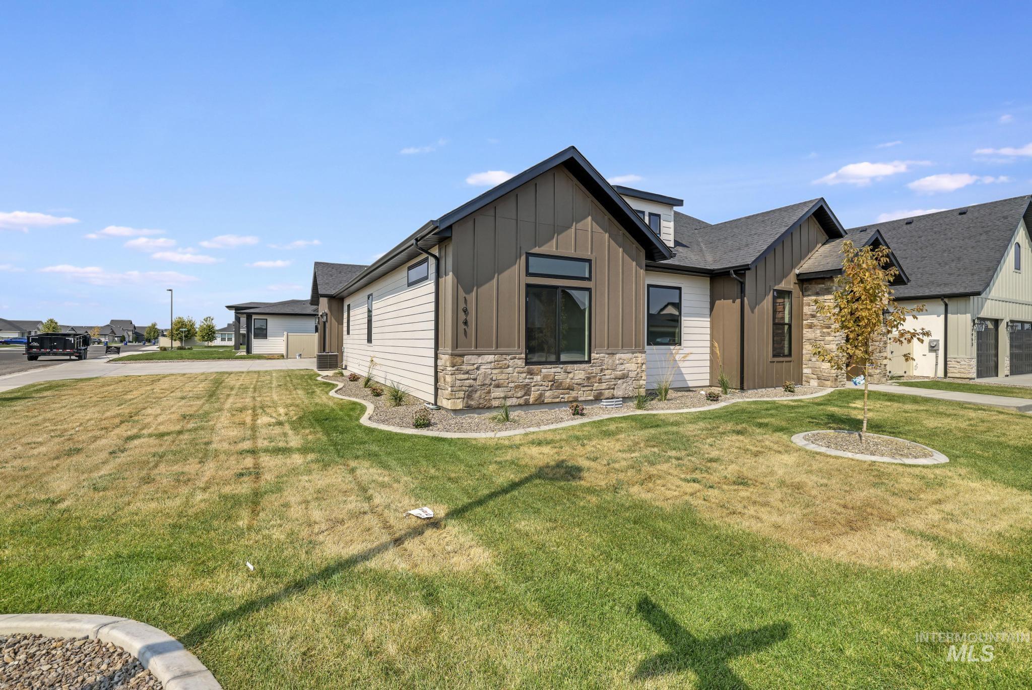 View of front of house featuring board and batten siding, stone siding, a front yard, a garage, and driveway