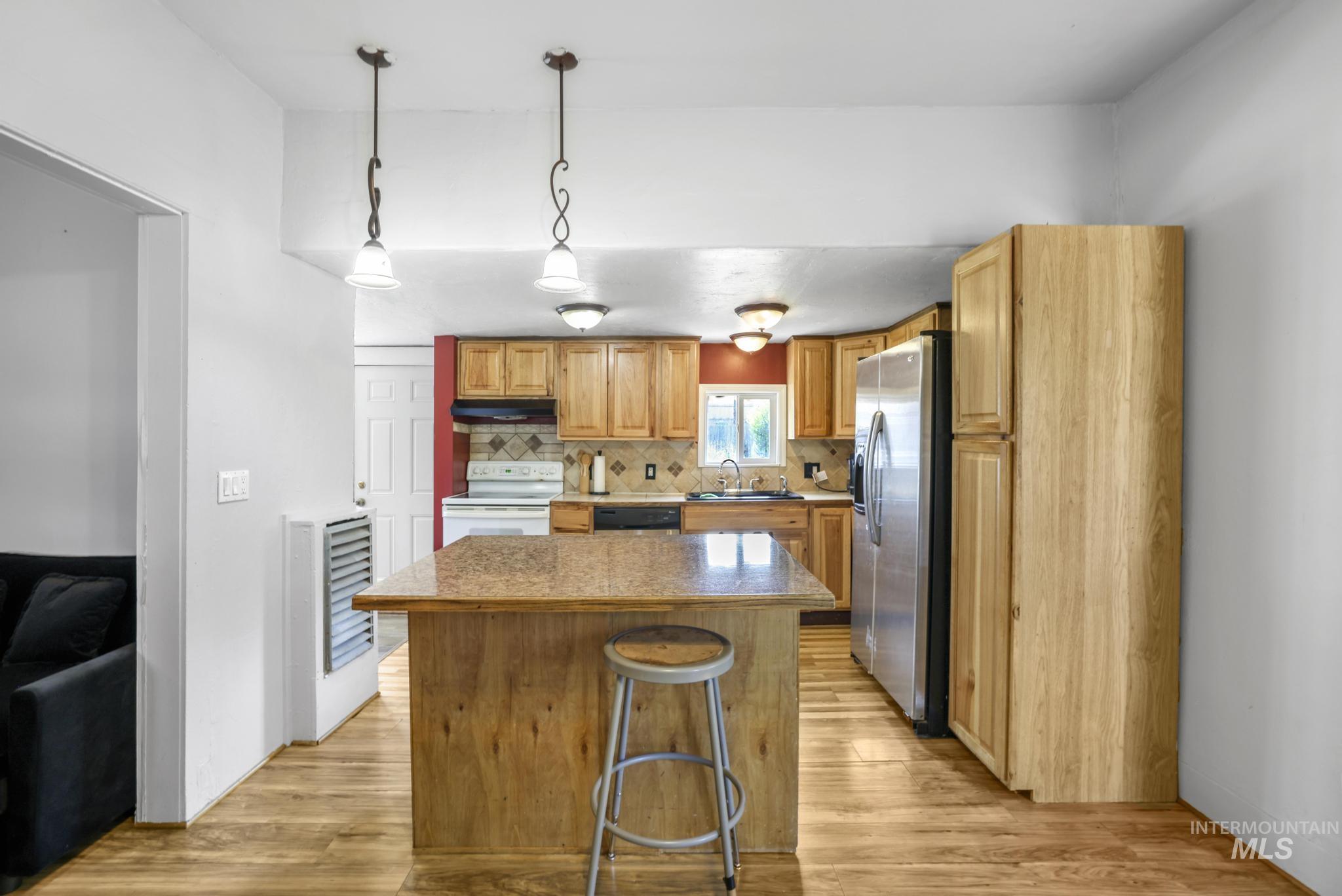 Kitchen featuring a kitchen island, tasteful backsplash, stainless steel appliances, light wood finished floors, and decorative light fixtures
