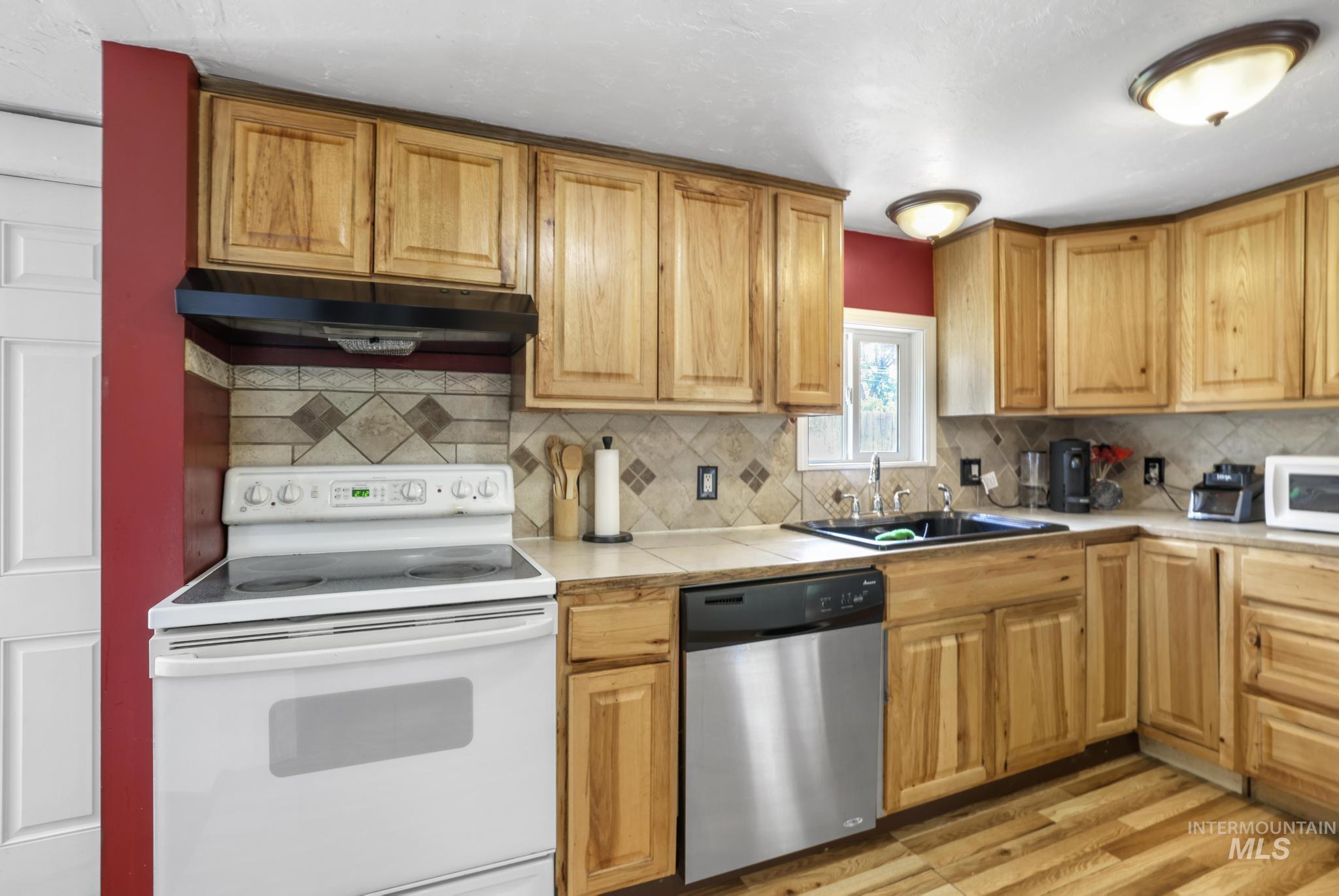 Kitchen featuring white appliances, under cabinet range hood, light wood-type flooring, and decorative backsplash