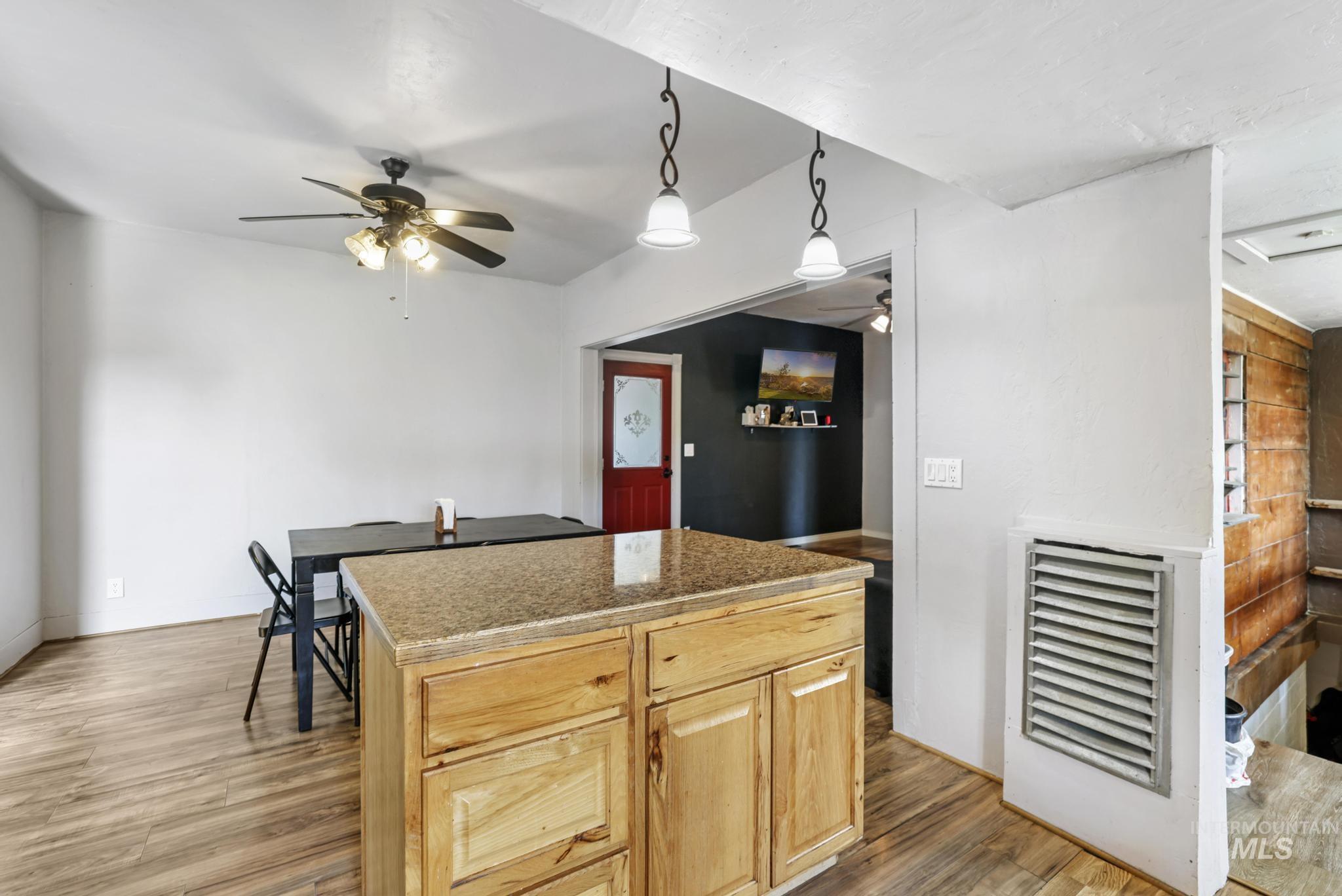 Kitchen with hanging light fixtures, light brown cabinetry, light wood-type flooring, a kitchen island, and a ceiling fan