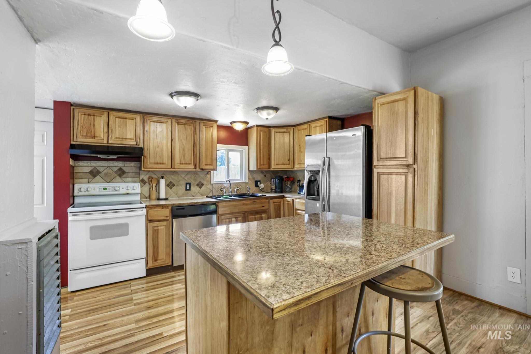 Kitchen featuring stainless steel appliances, pendant lighting, light wood-style floors, backsplash, and a kitchen breakfast bar