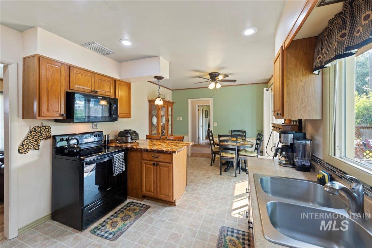 Kitchen featuring a peninsula, black appliances, brown cabinetry, hanging light fixtures, and recessed lighting