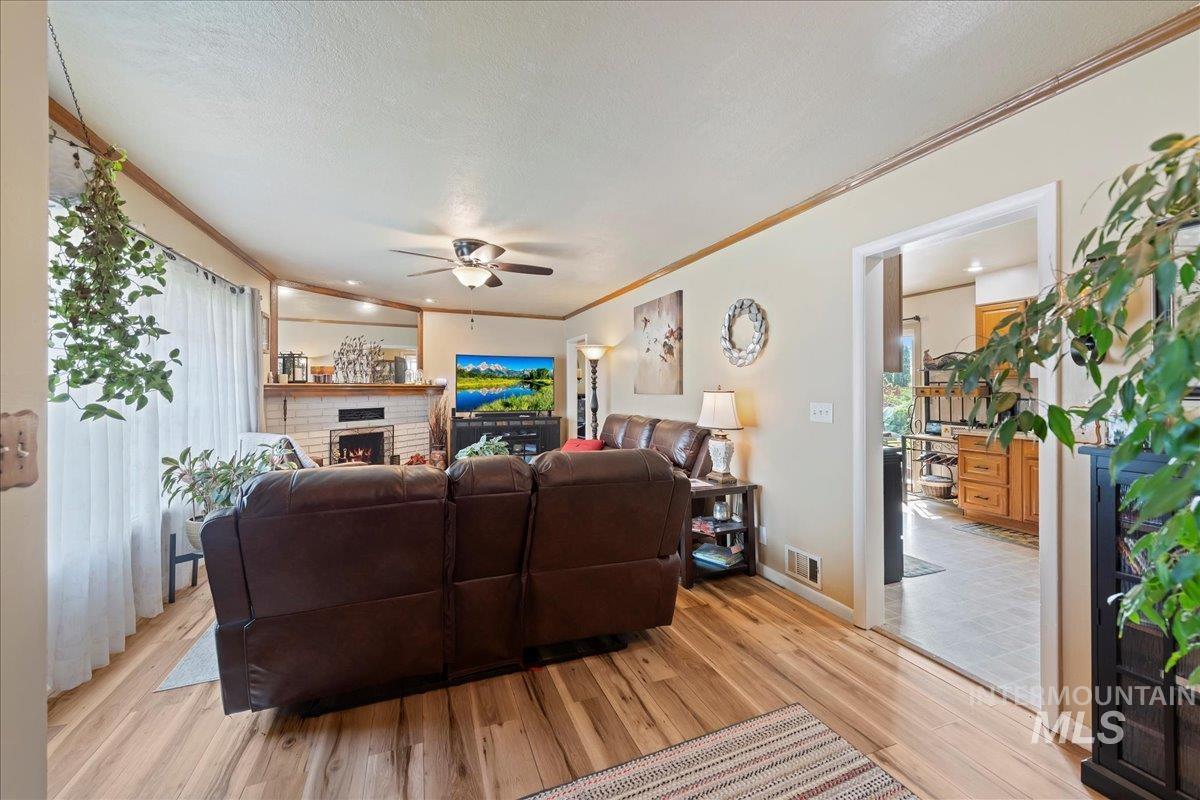Living area with ornamental molding, light wood-style floors, a fireplace, ceiling fan, and a textured ceiling
