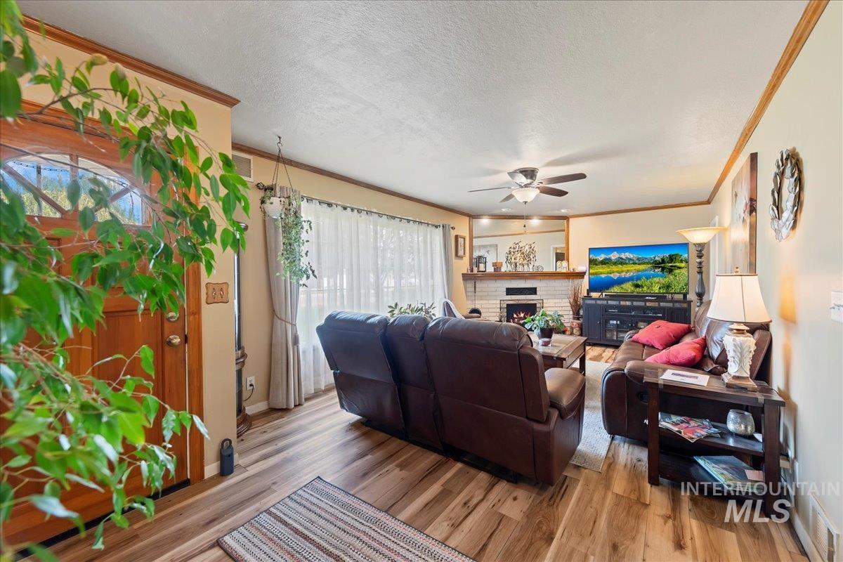 Living area featuring a textured ceiling, crown molding, a fireplace, light wood-style floors, and ceiling fan