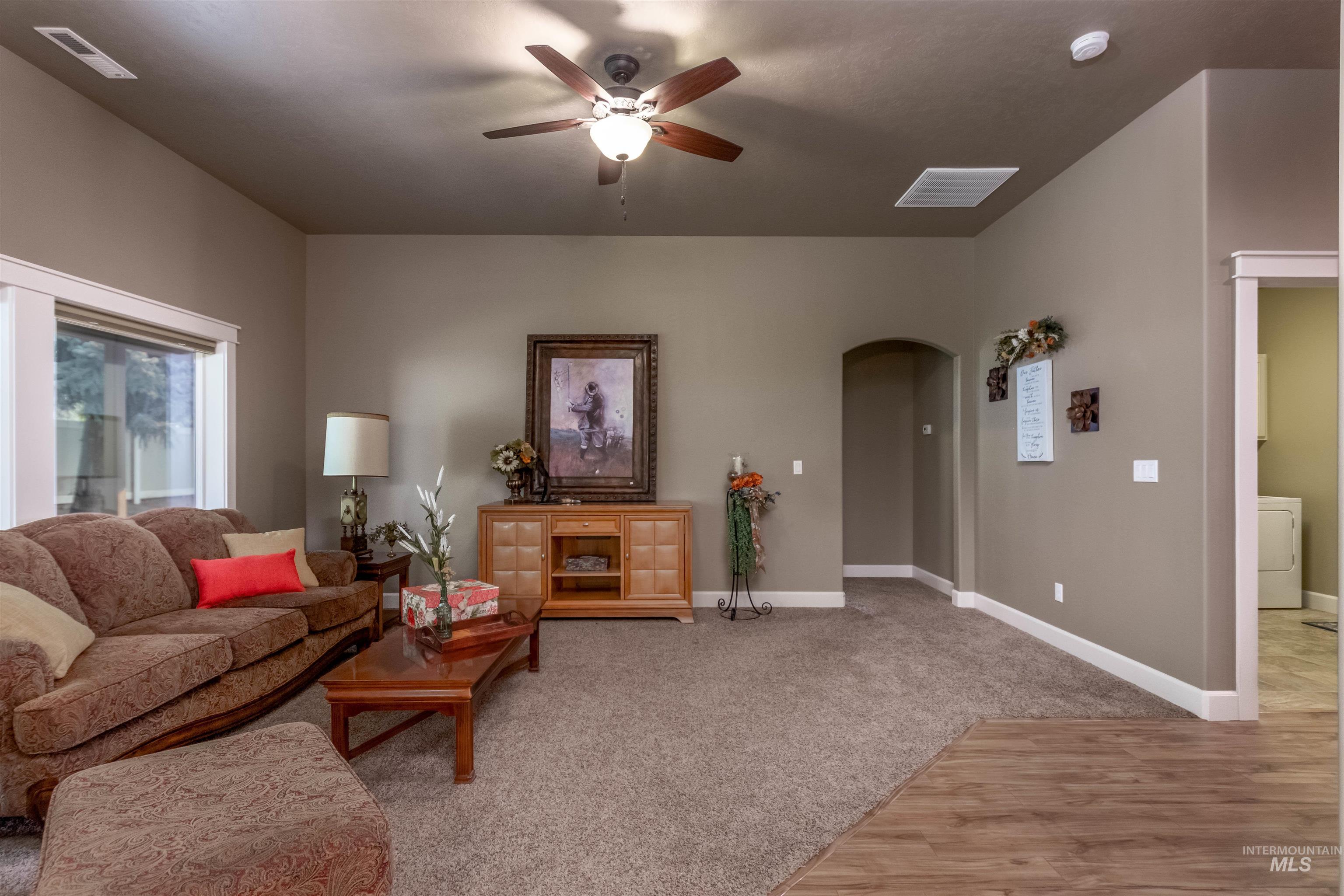 Living room with arched walkways, light wood-style flooring, a ceiling fan, washer / clothes dryer, and light colored carpet