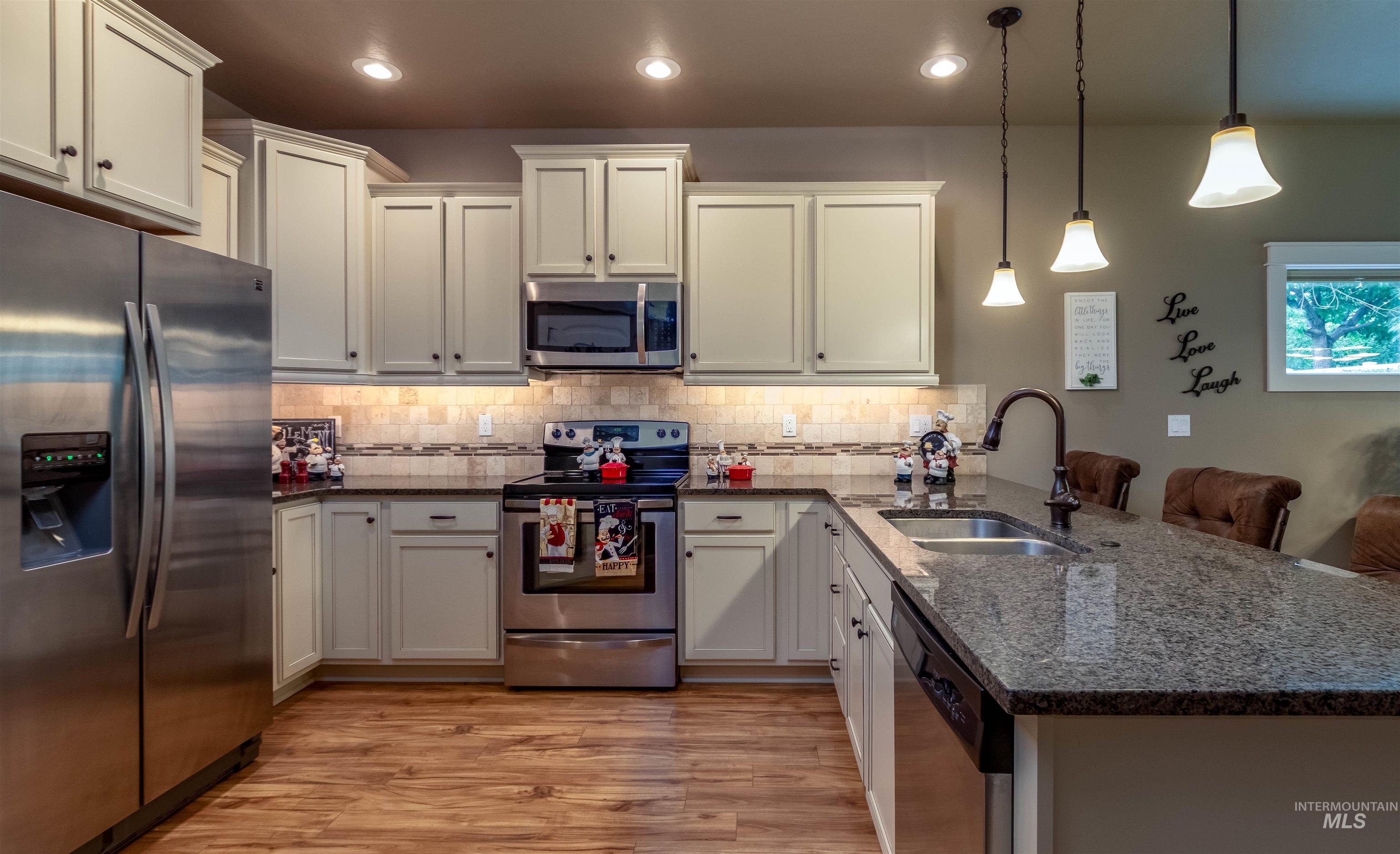 Kitchen with stainless steel appliances, a peninsula, dark stone countertops, pendant lighting, and light wood-style flooring