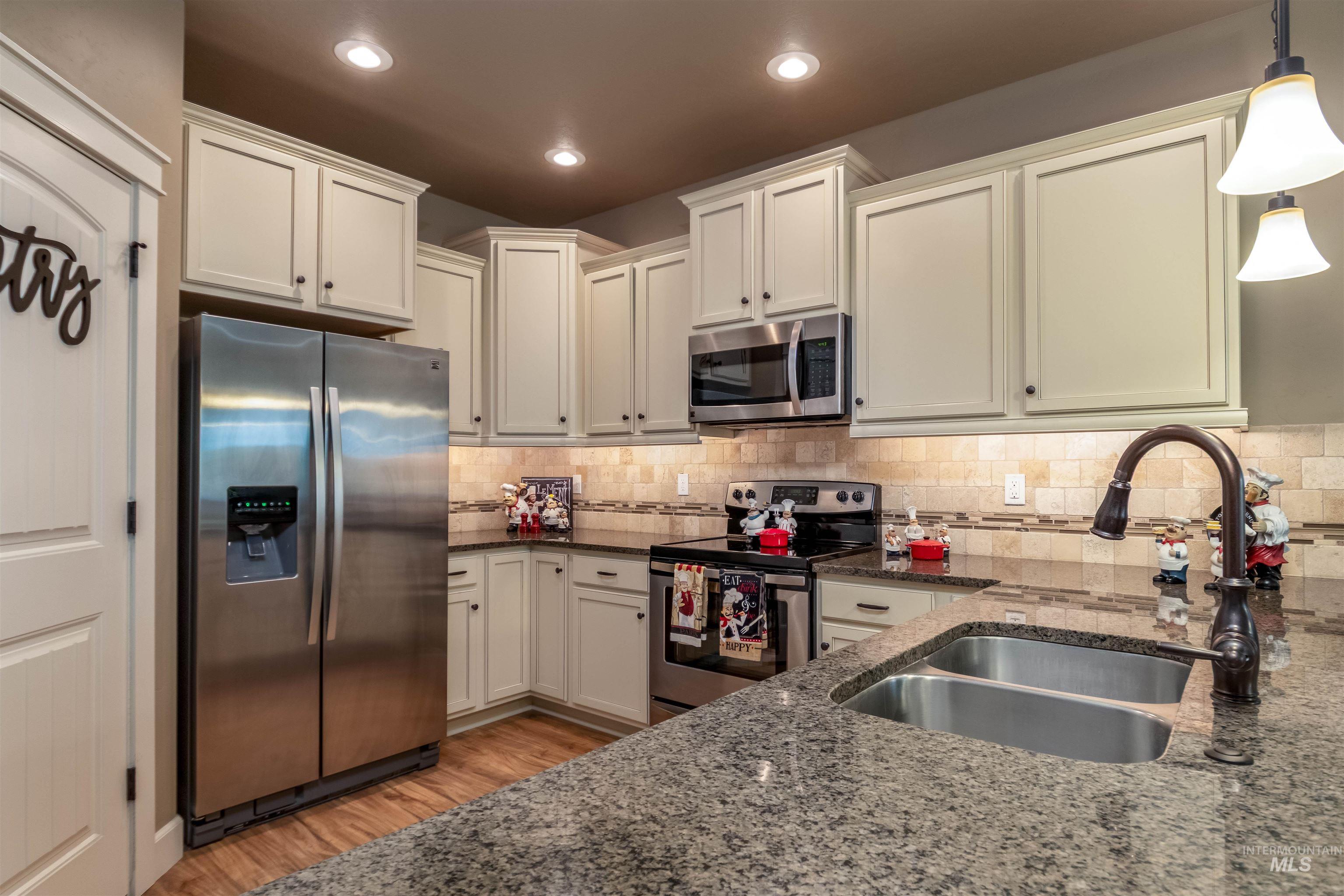 Kitchen featuring stainless steel appliances, dark stone counters, tasteful backsplash, light wood-type flooring, and pendant lighting