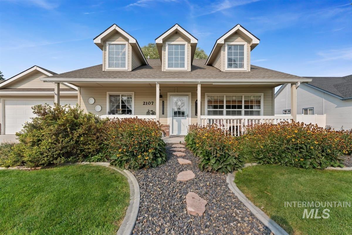 View of front of property with covered porch, a shingled roof, a front lawn, and a garage